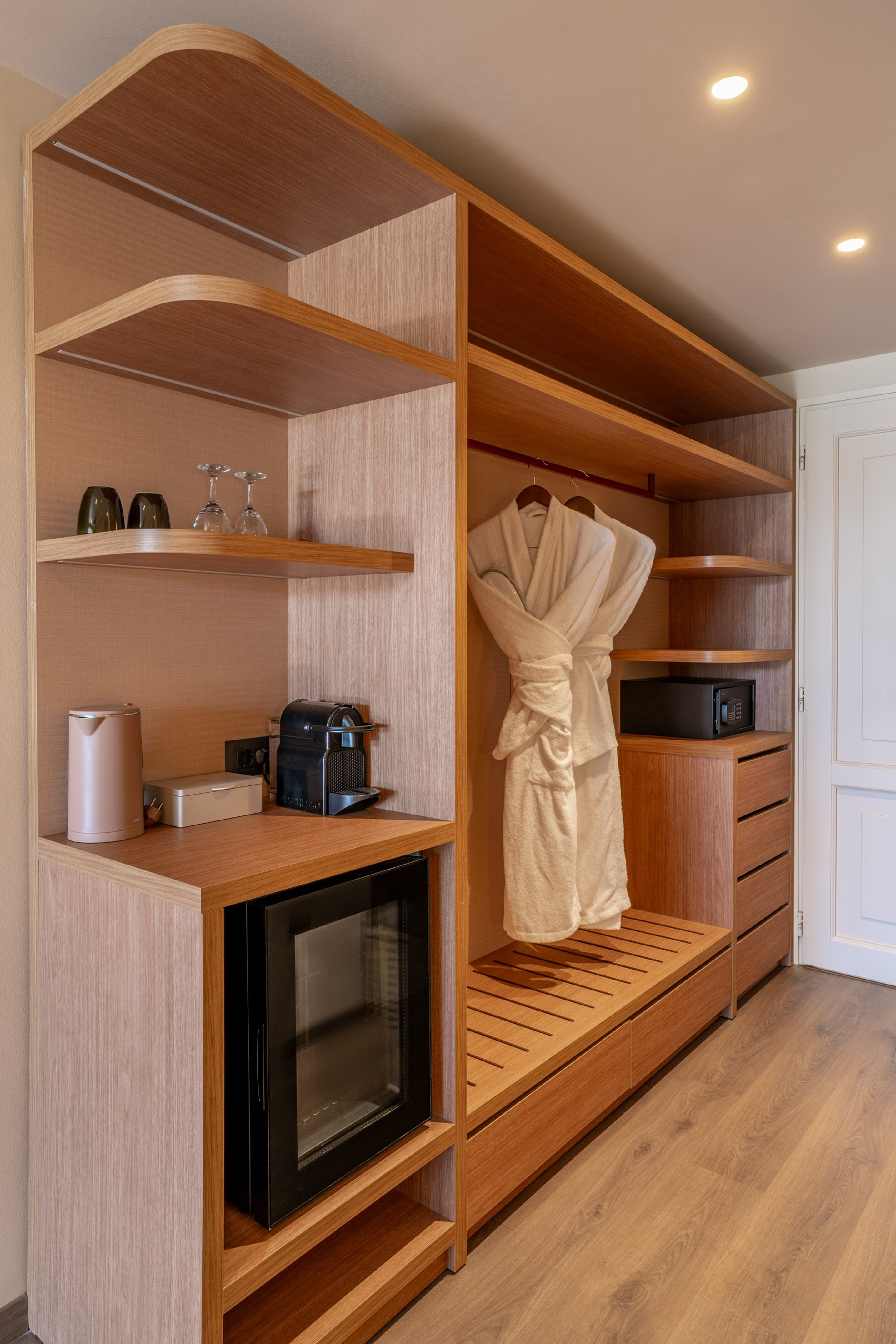 Modern hotel wardrobe with mini-bar, Nespresso, safe, and bathrobes.