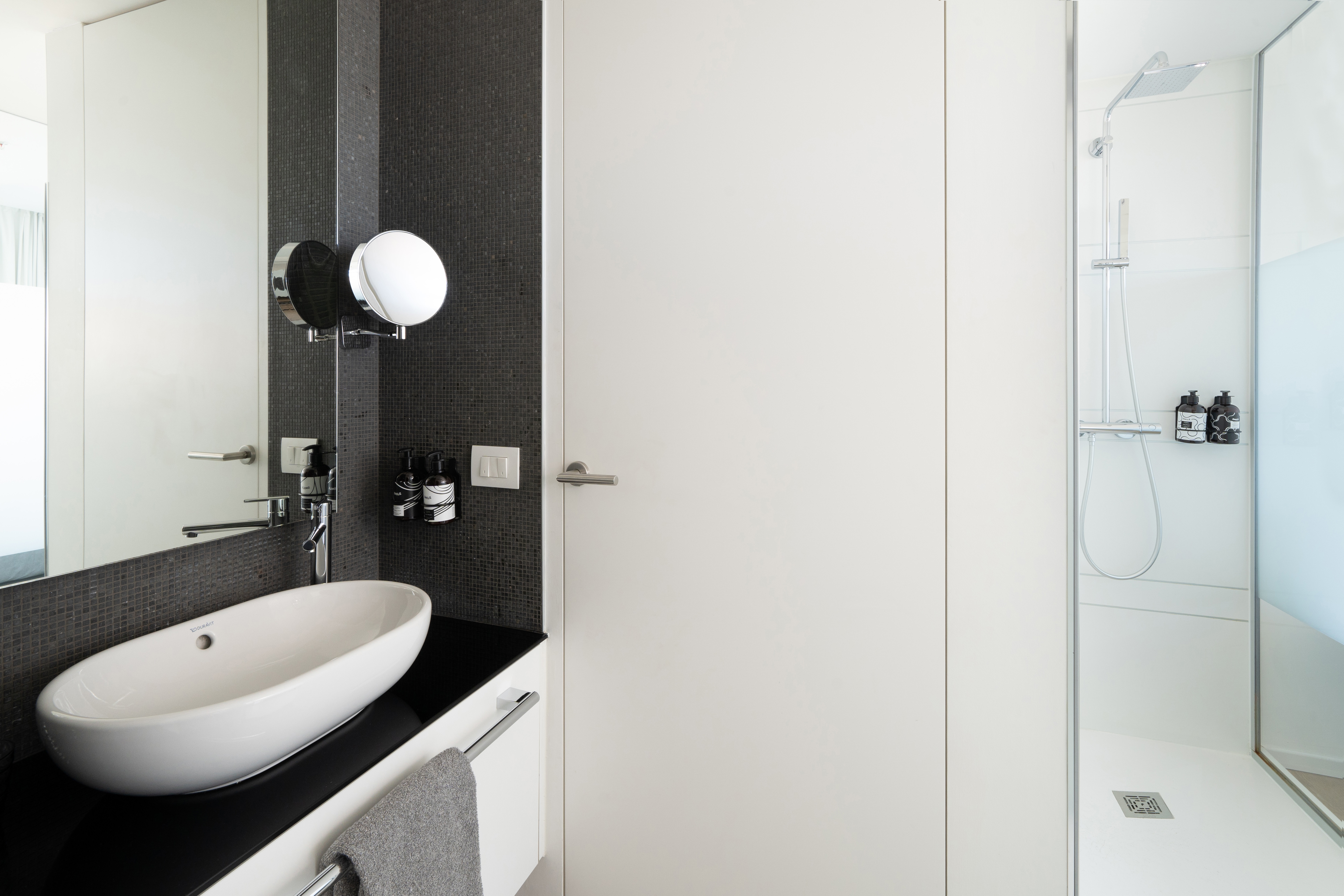 Modern bathroom with white vessel sink, black mosaic tiles, and walk-in shower.
