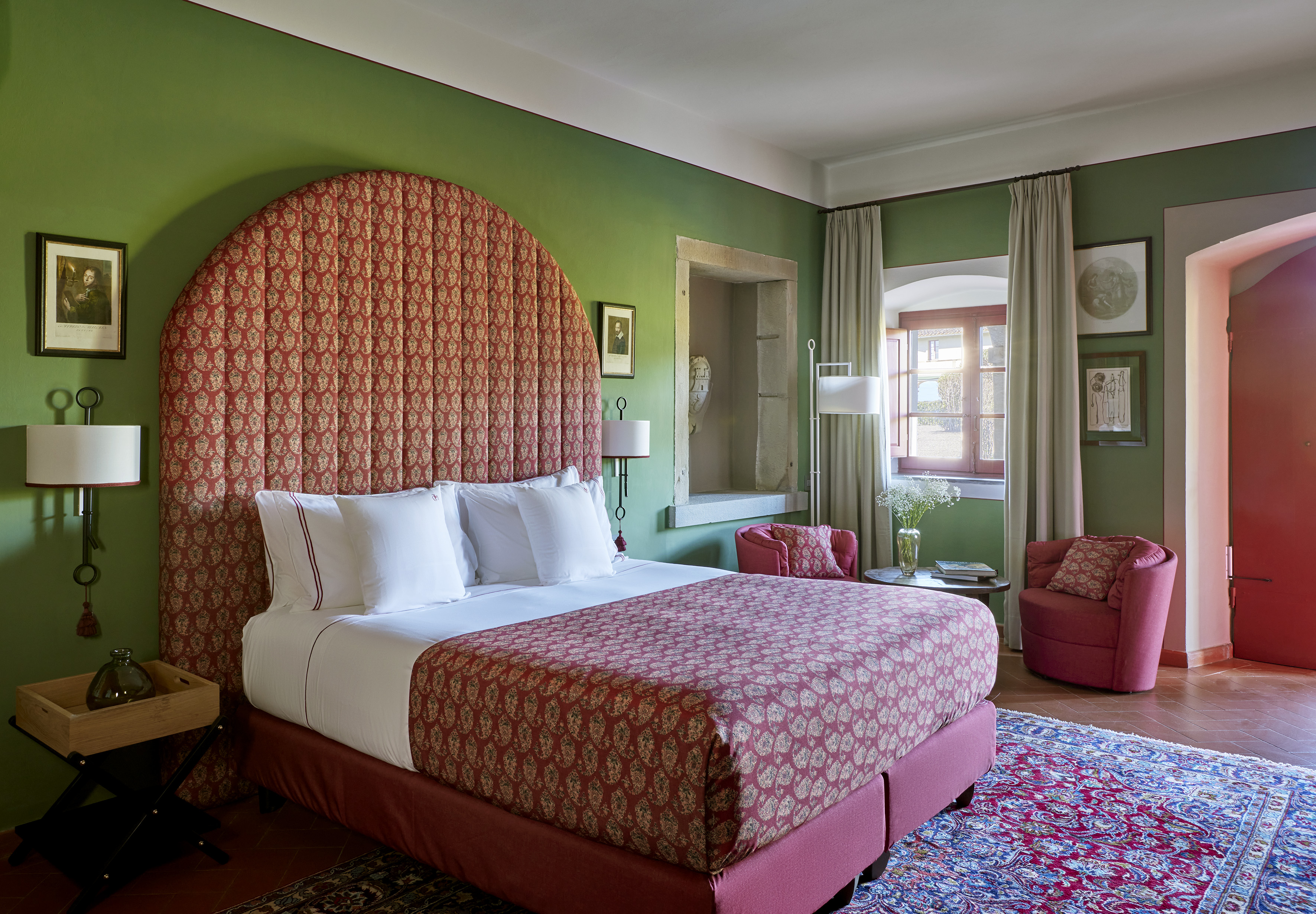Hotel room with green walls, red patterned bed, and colourful accent rug.