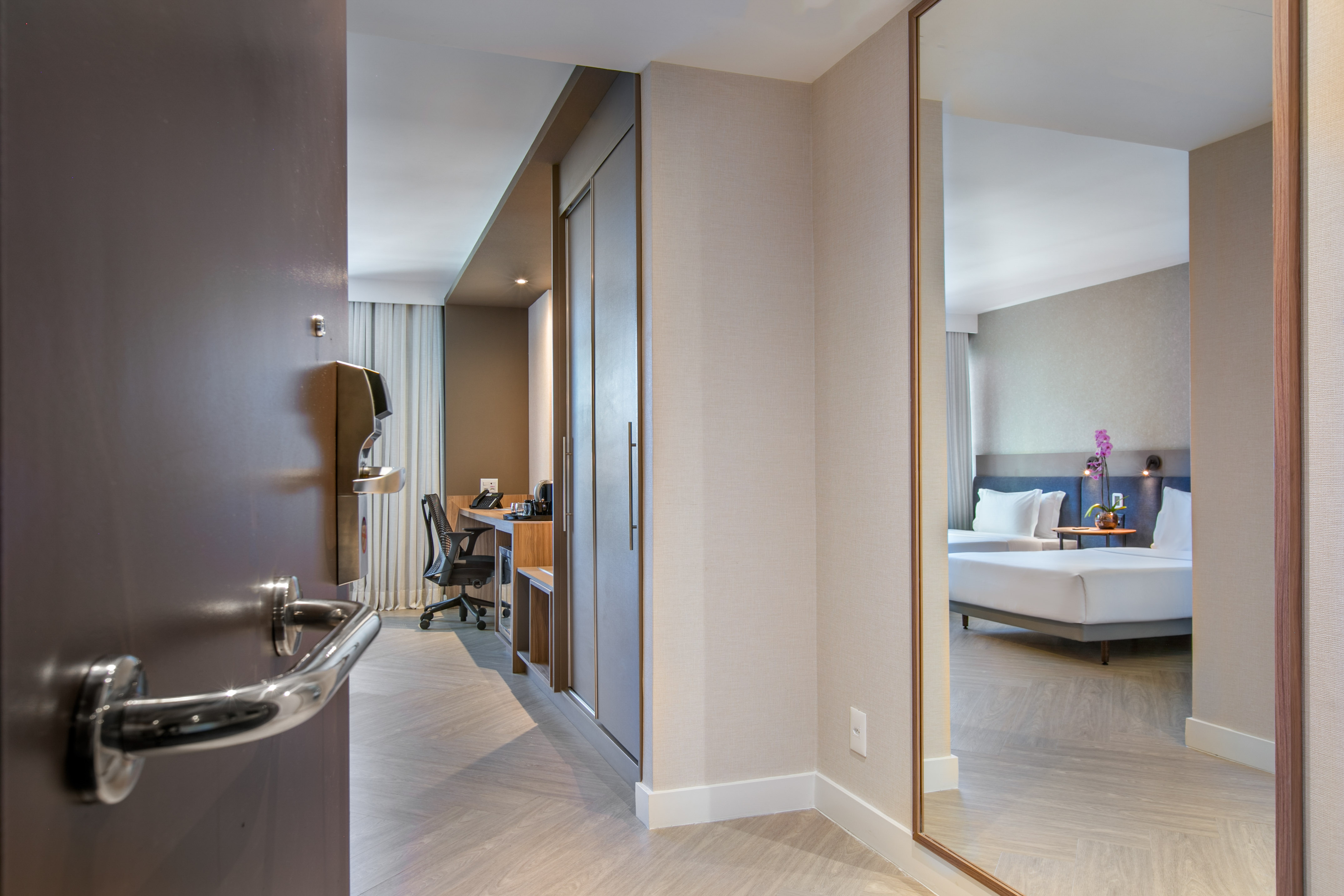 Modern hotel room entrance showing desk, closet, and bedroom in mirror.