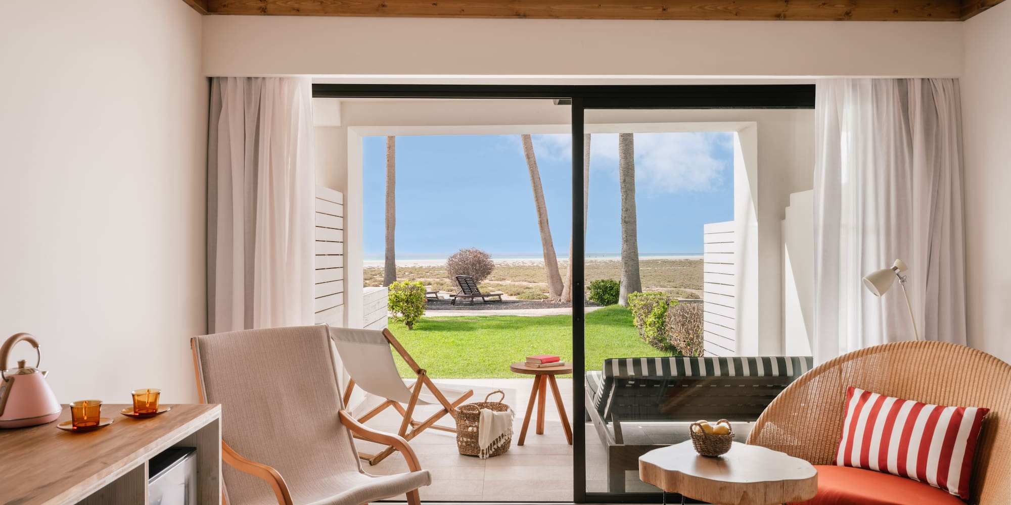 Suite moderna con terraza a la playa, palmeras y mar. Sillas de mimbre.