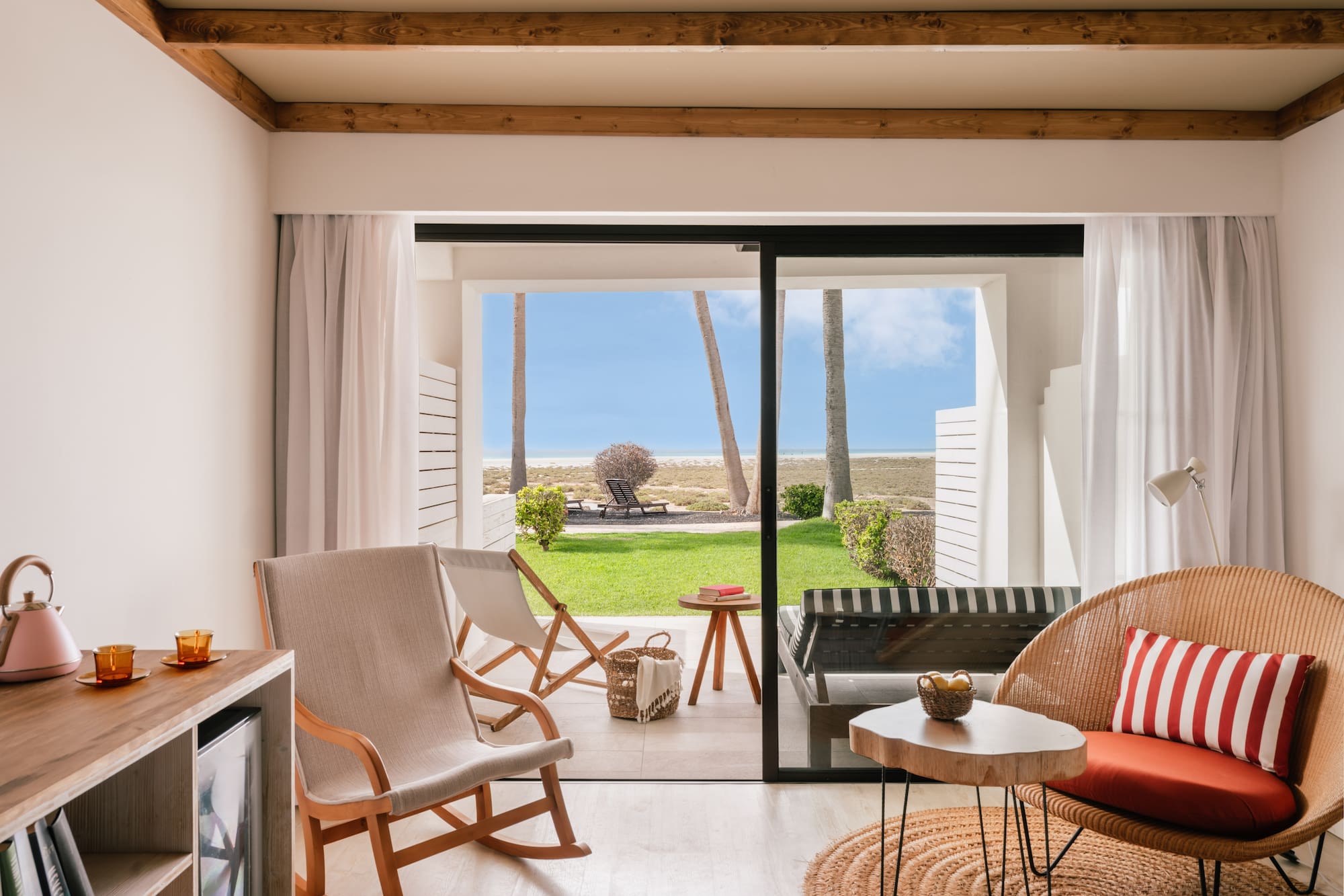 Suite moderna con terraza a la playa, palmeras y mar. Sillas de mimbre.