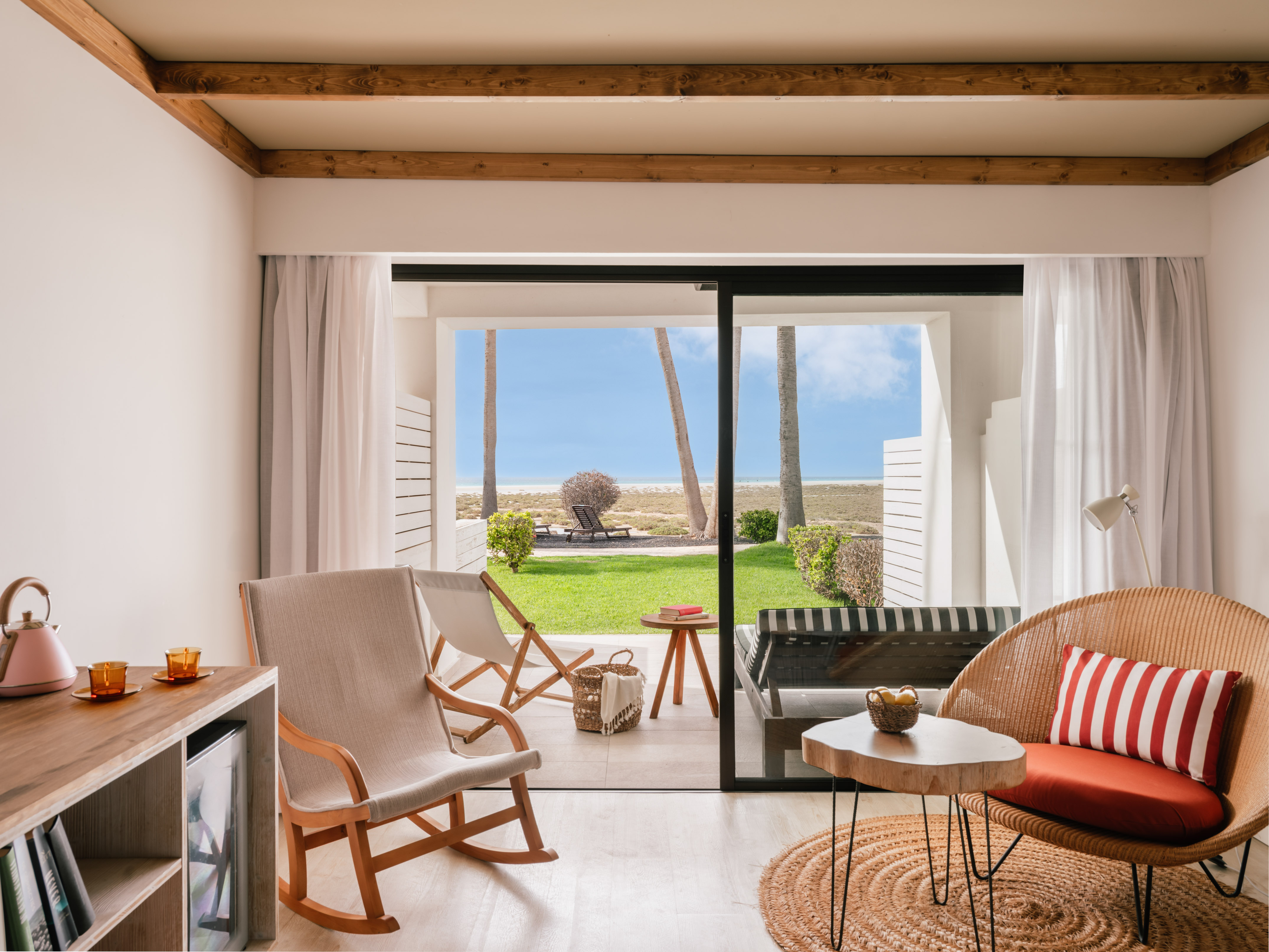 Suite moderna con terraza a la playa, palmeras y mar. Sillas de mimbre.