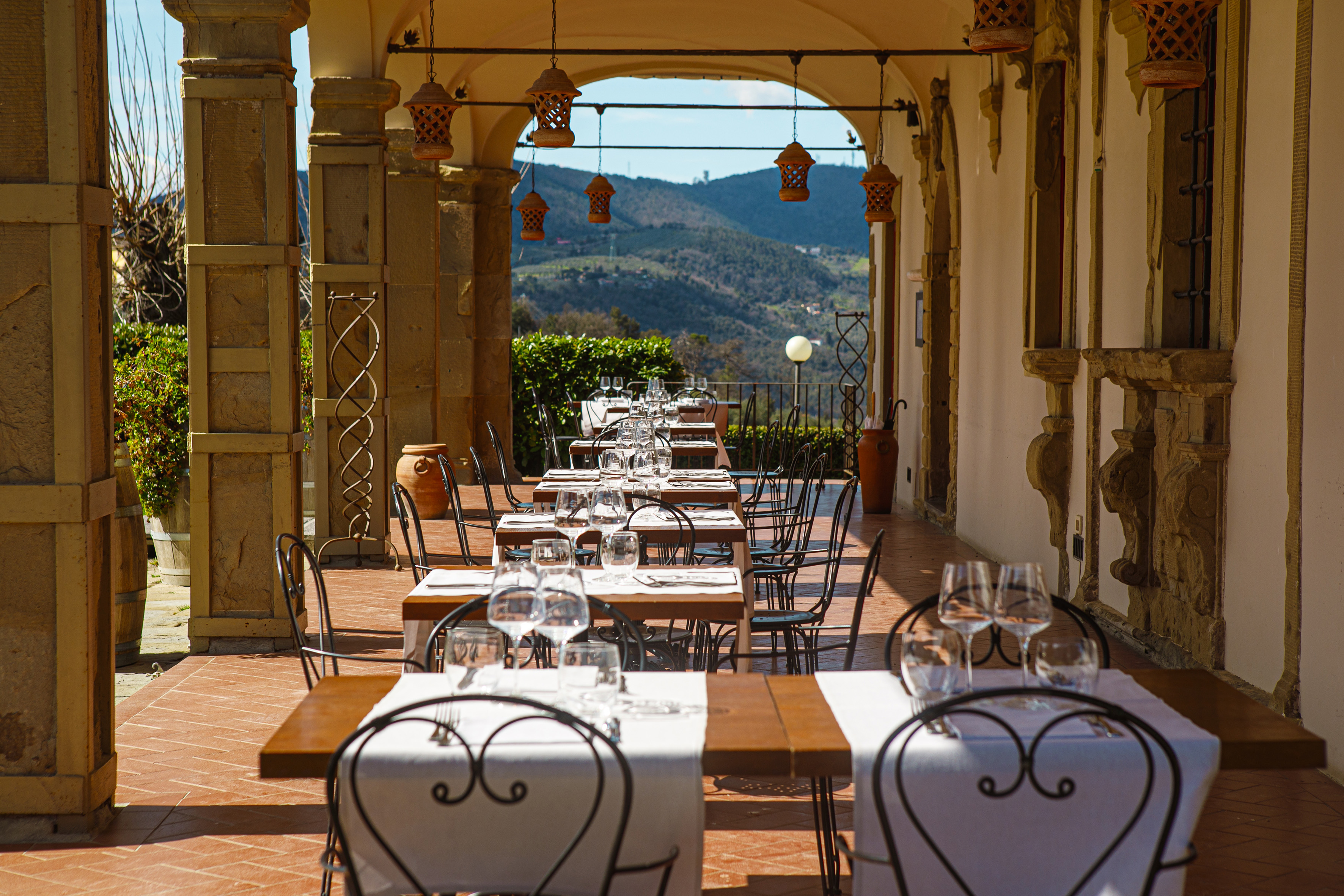 Outdoor restaurant terrace with set tables, hanging lanterns, and mountain view.
