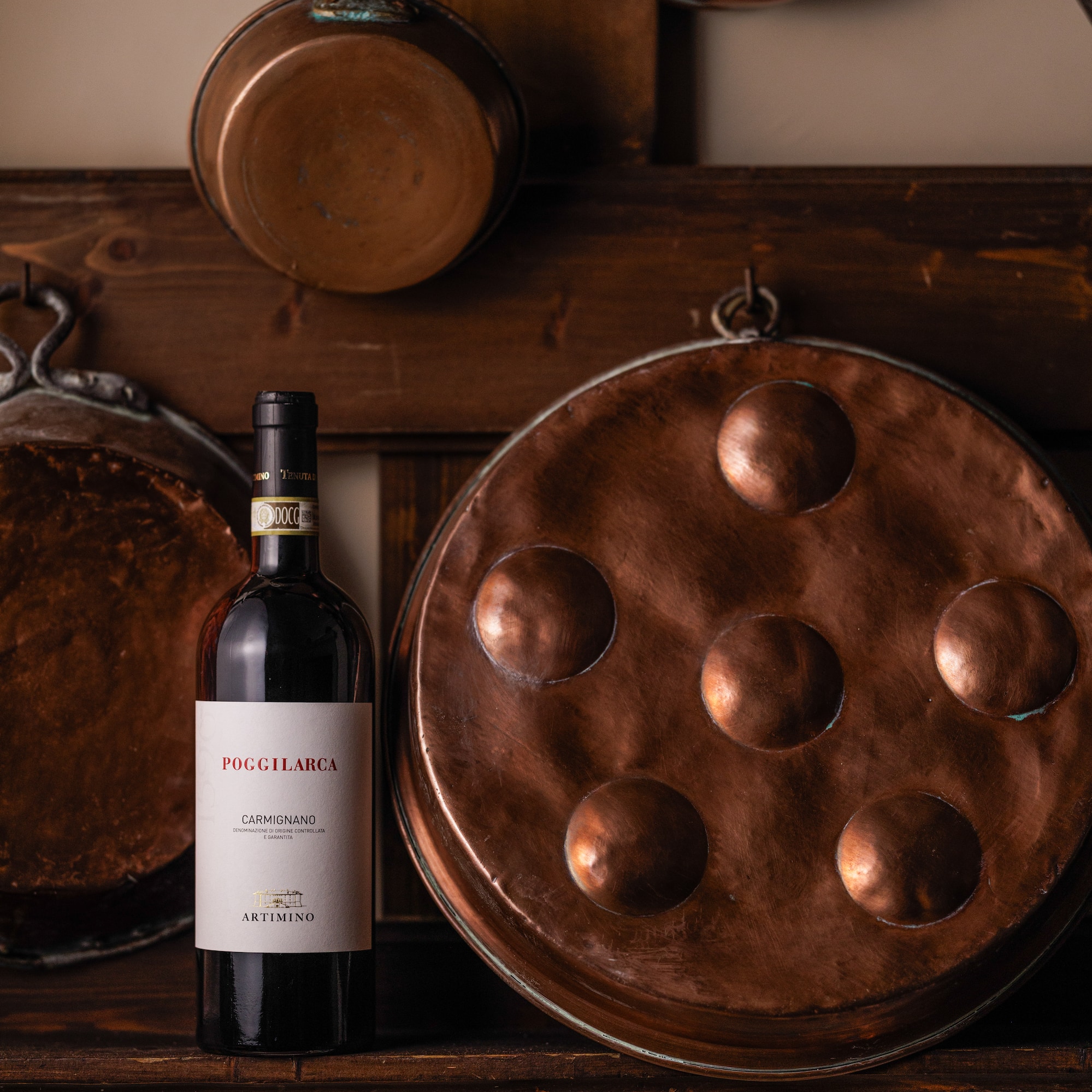 Poggilarca Carmignano red wine bottle, vintage copper pots, rustic shelf.