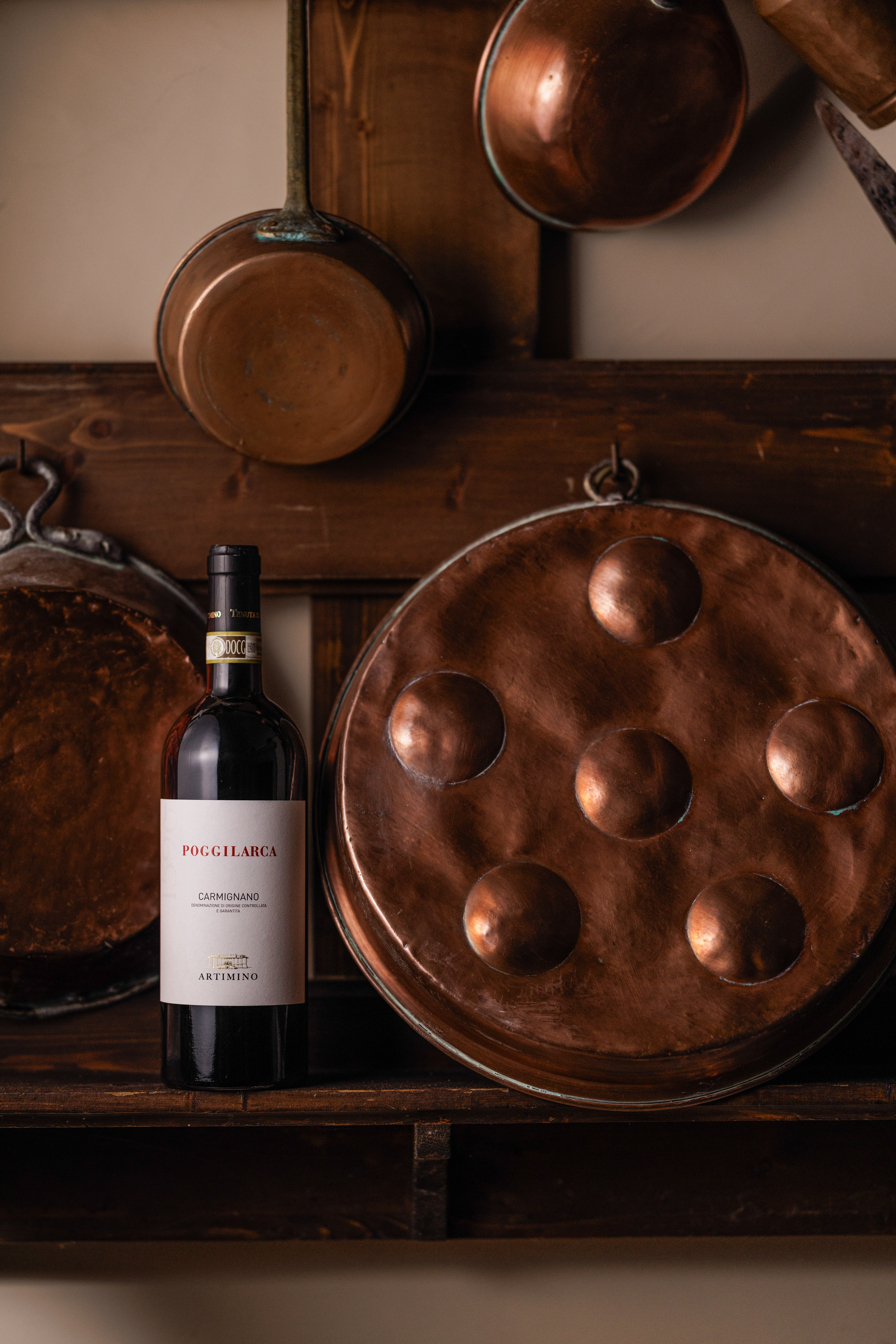 Poggilarca Carmignano red wine bottle, vintage copper pots, rustic shelf.