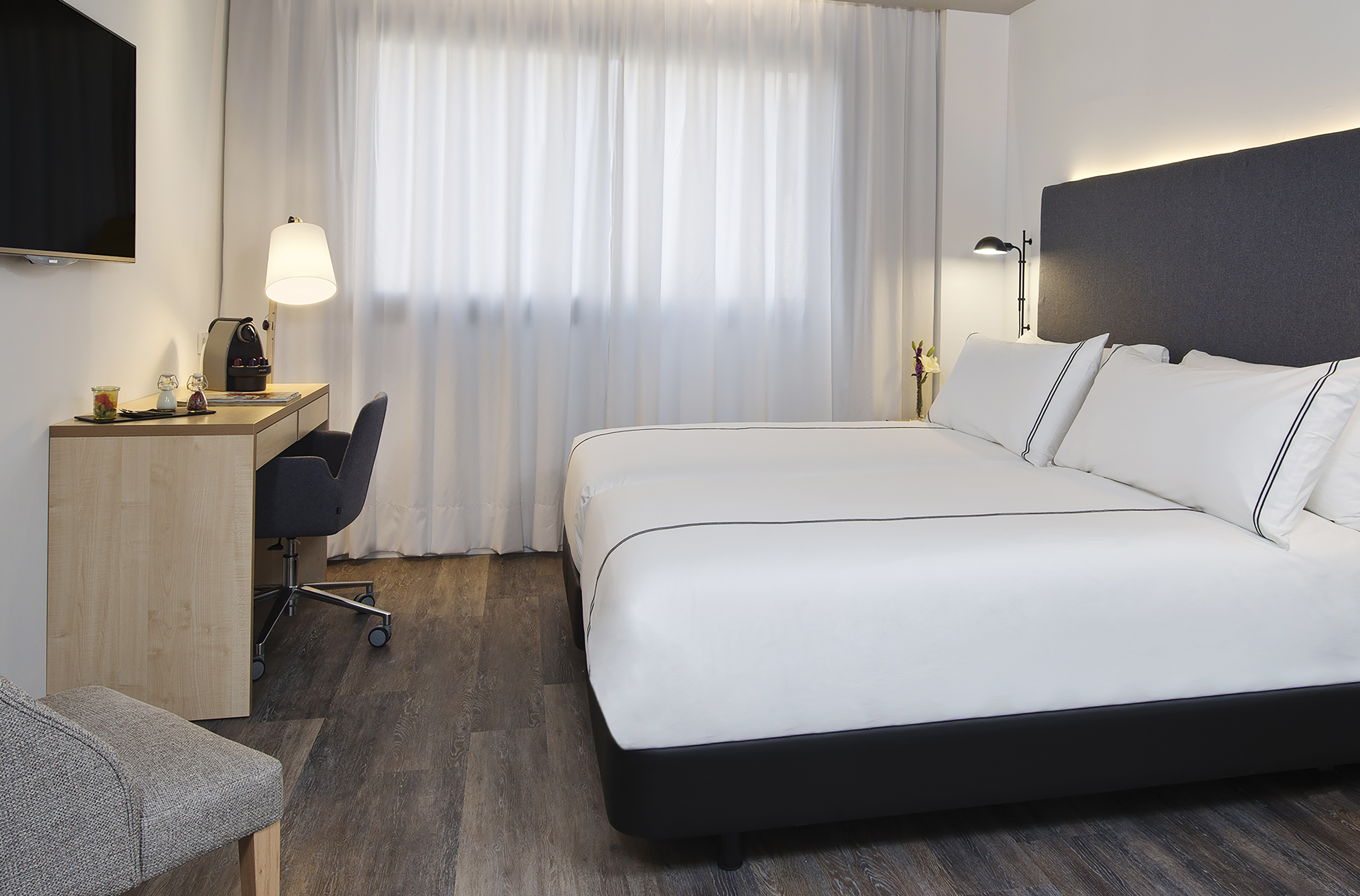 Clean modern hotel room with king bed, workspace, and sheer curtains.