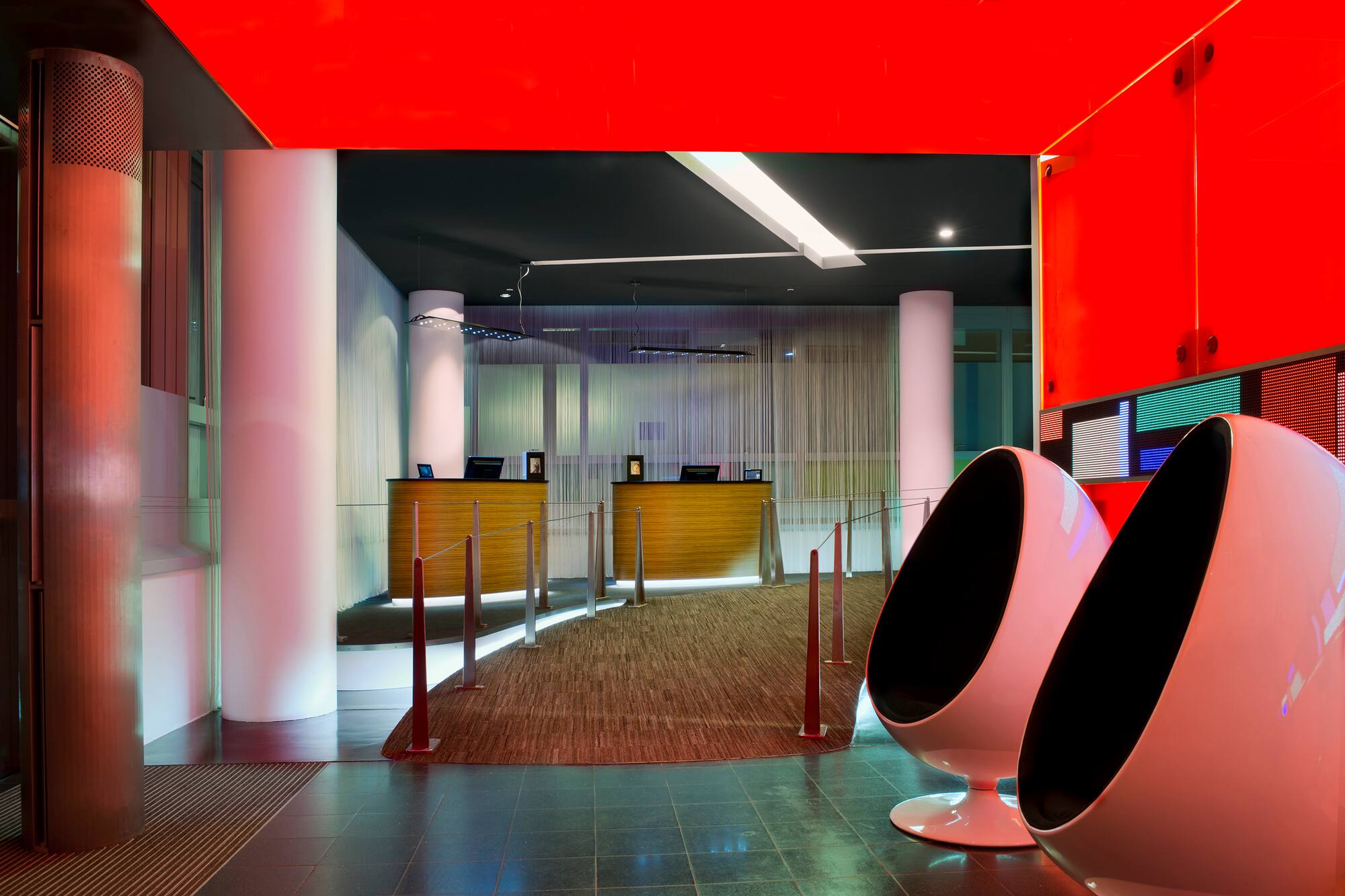 Modern hotel lobby with red ceiling, two reception desks, and white egg chairs.