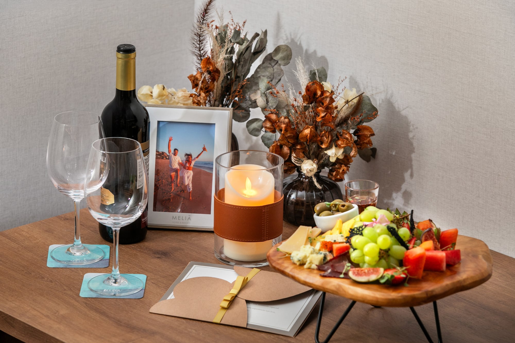 Amenidad Meliá: vino, copas, tabla de quesos/frutas, vela y foto en mesa.
