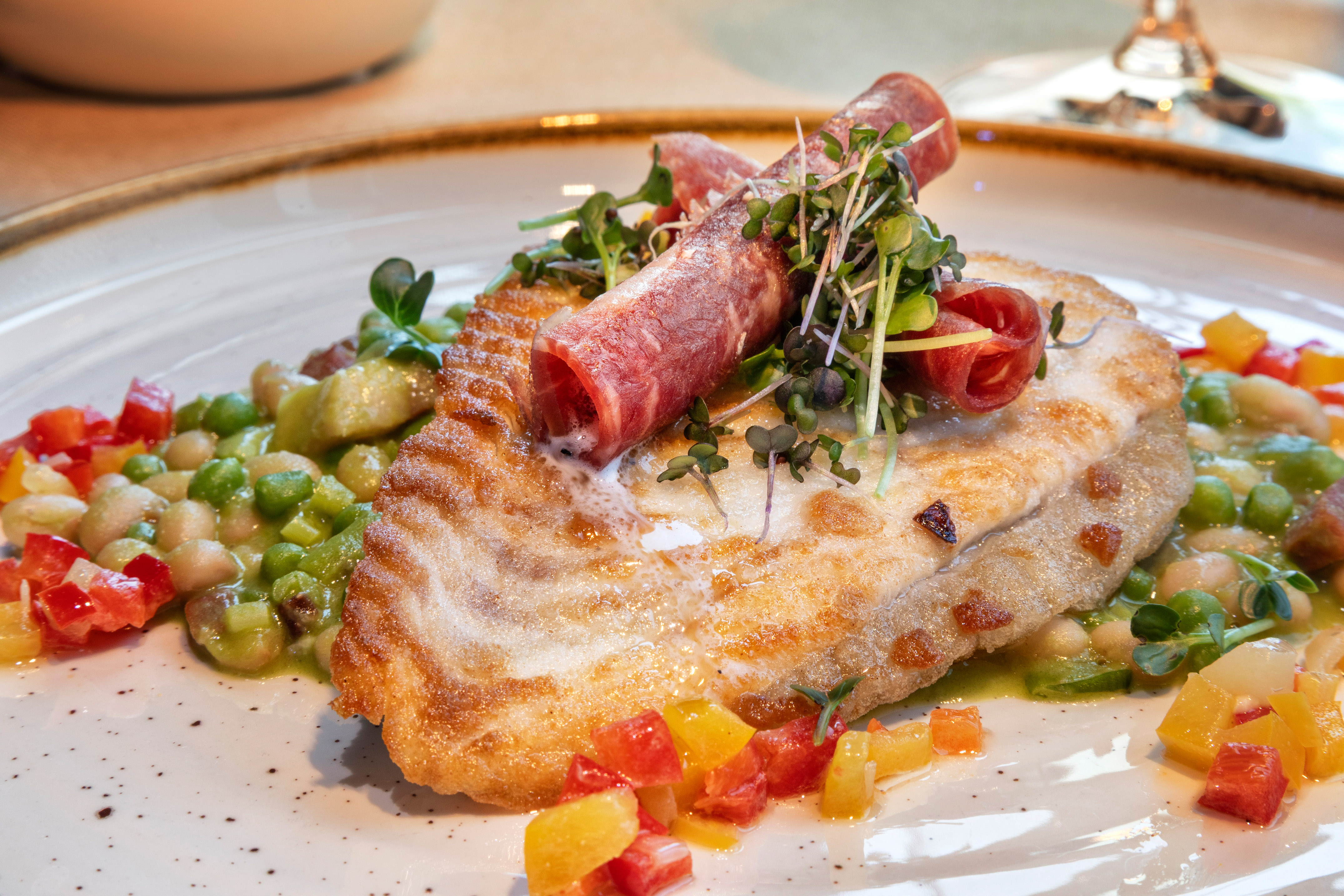 Pan-fried fish fillet, prosciutto, microgreens, peas, beans, colorful peppers.