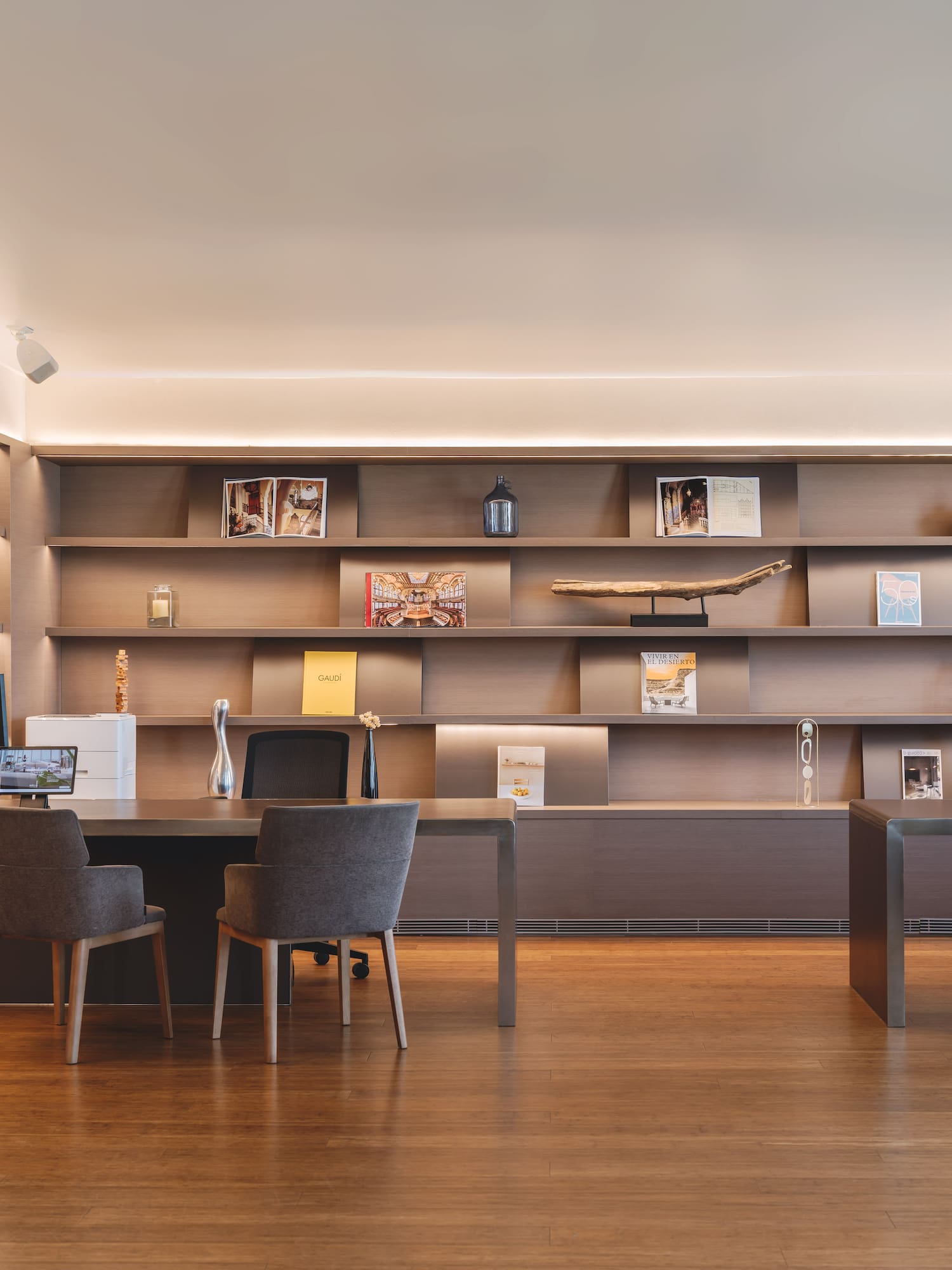 Modern office interior with wooden desks, chairs, illuminated shelves, and plant.