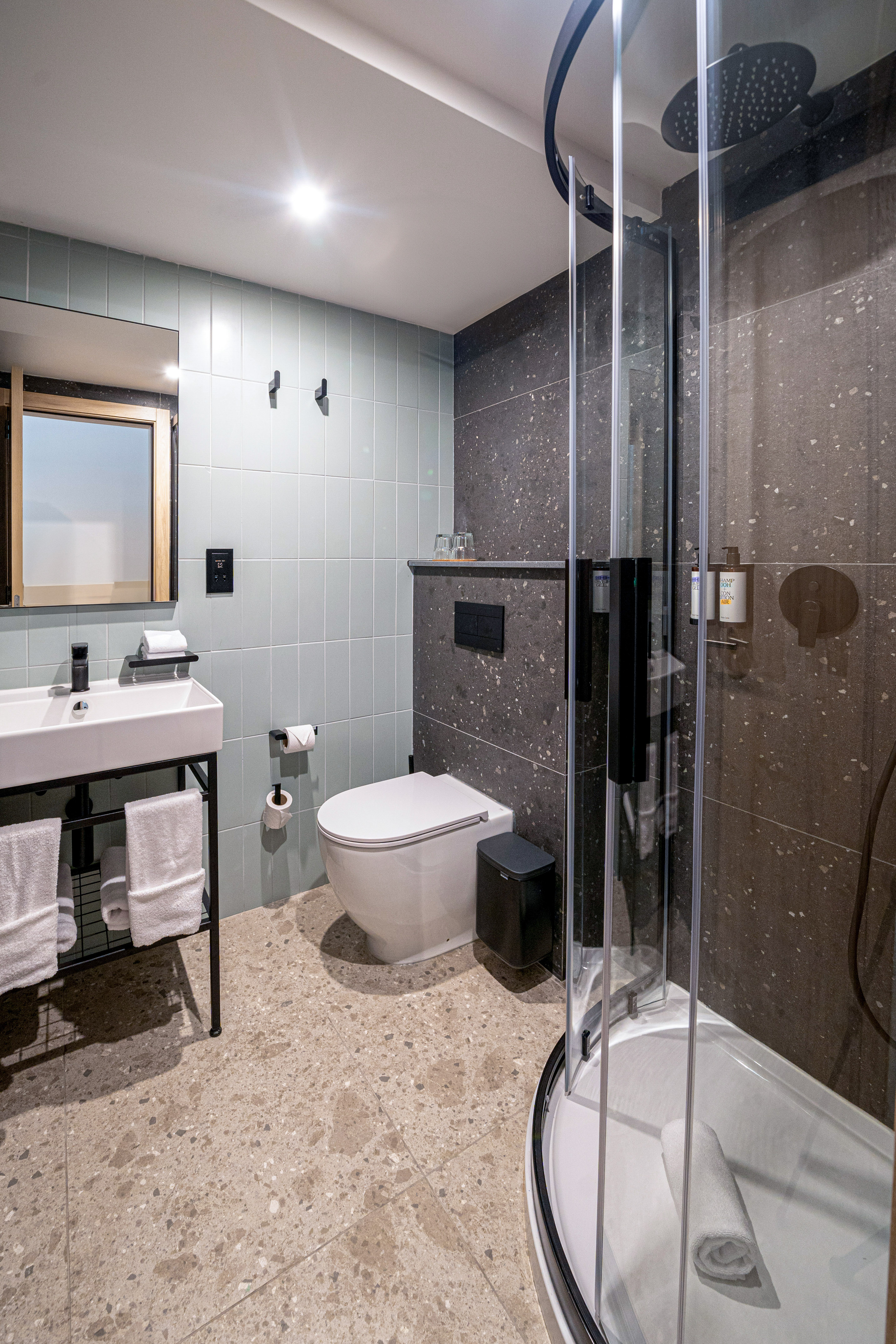 Modern hotel bathroom with white sink, toilet, glass shower, and terrazzo floor.