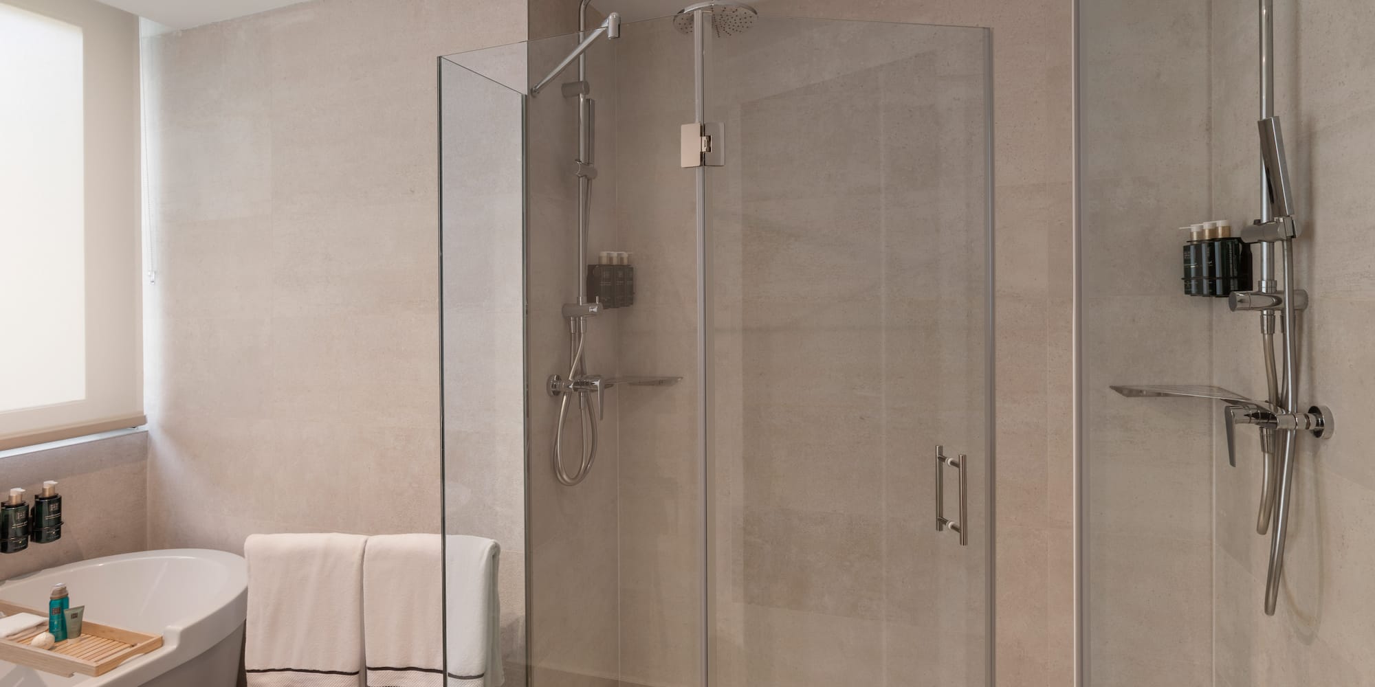Baño moderno con ducha de cristal, bañera, azulejos claros y toallas.