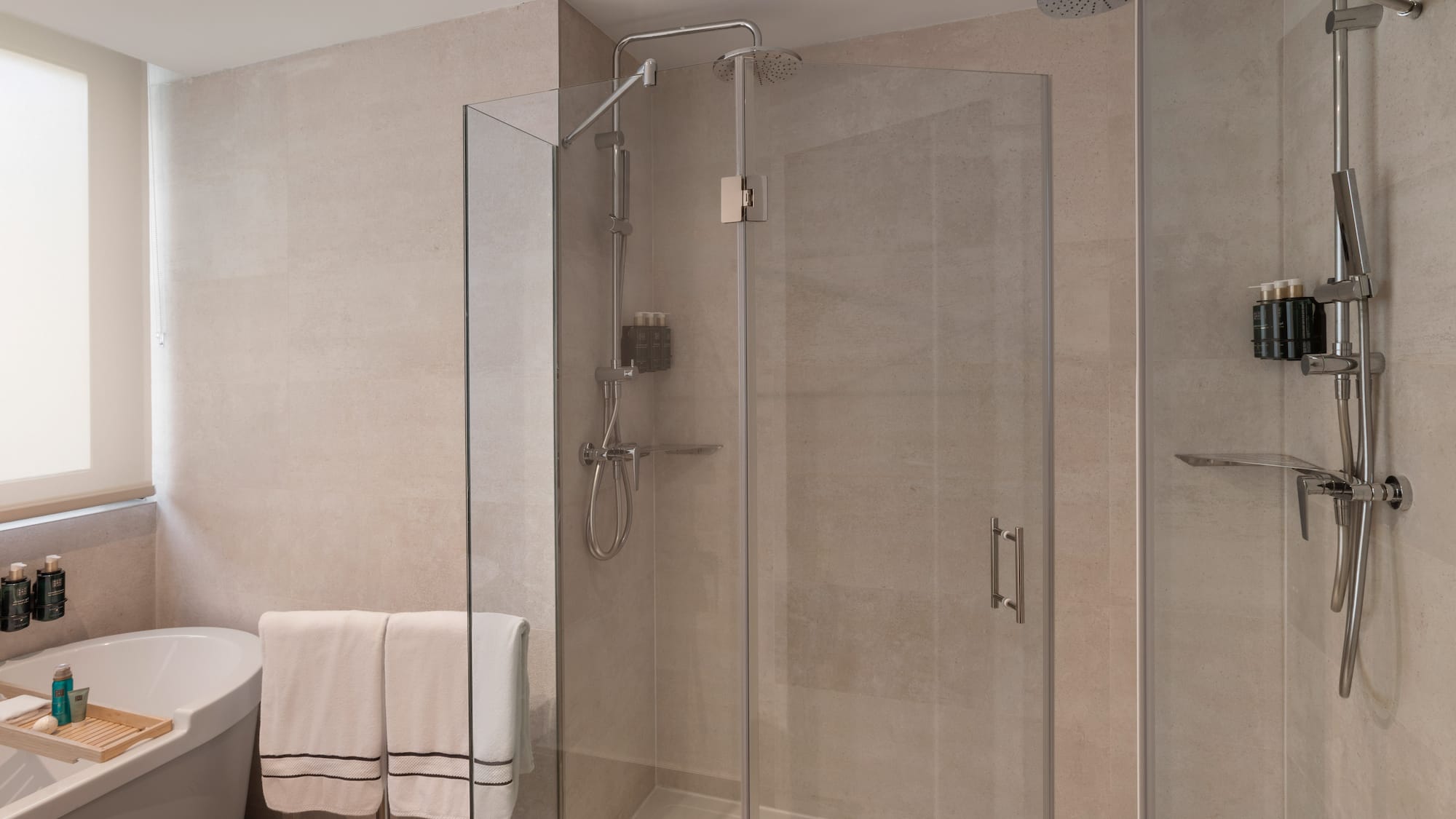 Baño moderno con ducha de cristal, bañera, azulejos claros y toallas.