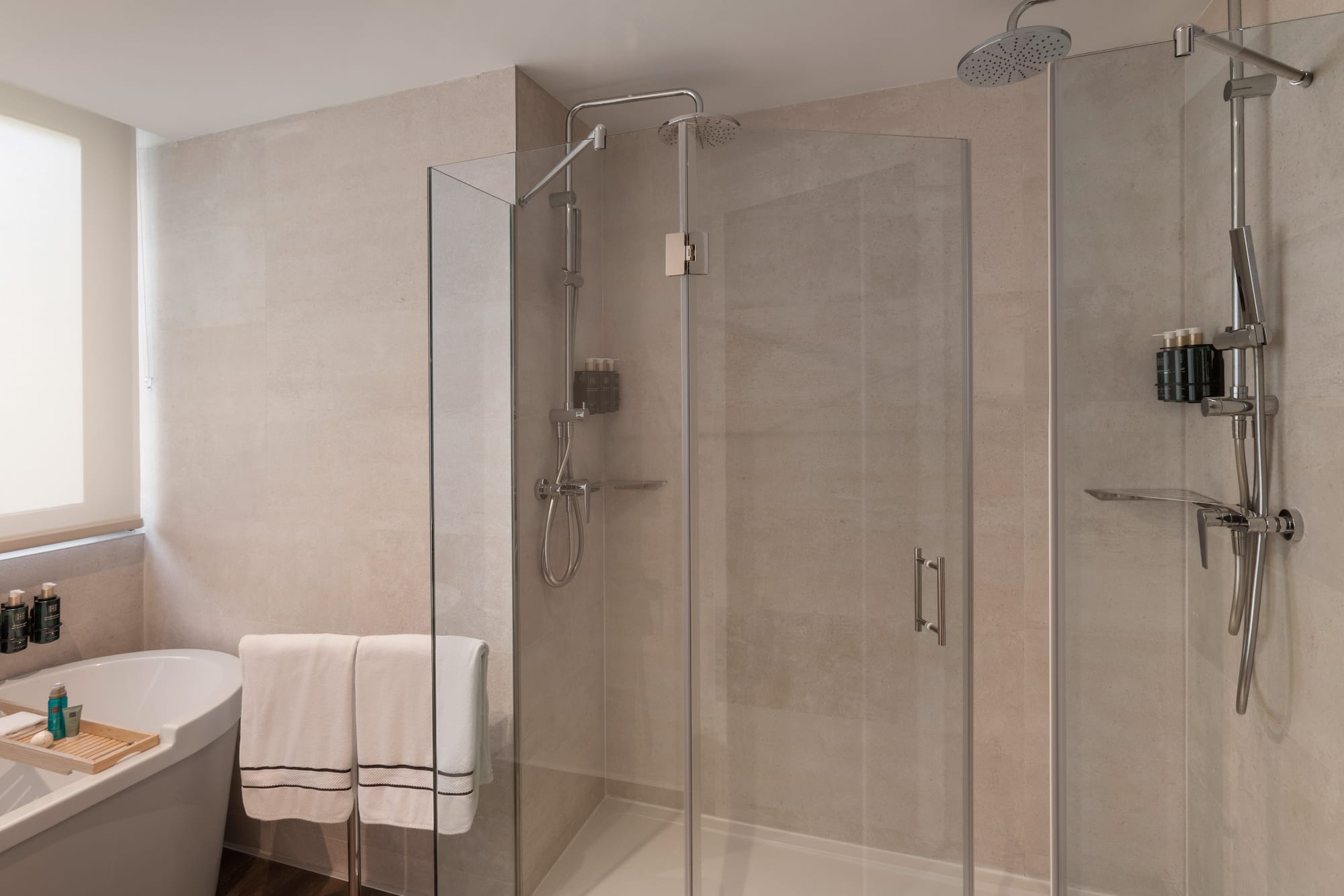 Baño moderno con ducha de cristal, bañera, azulejos claros y toallas.
