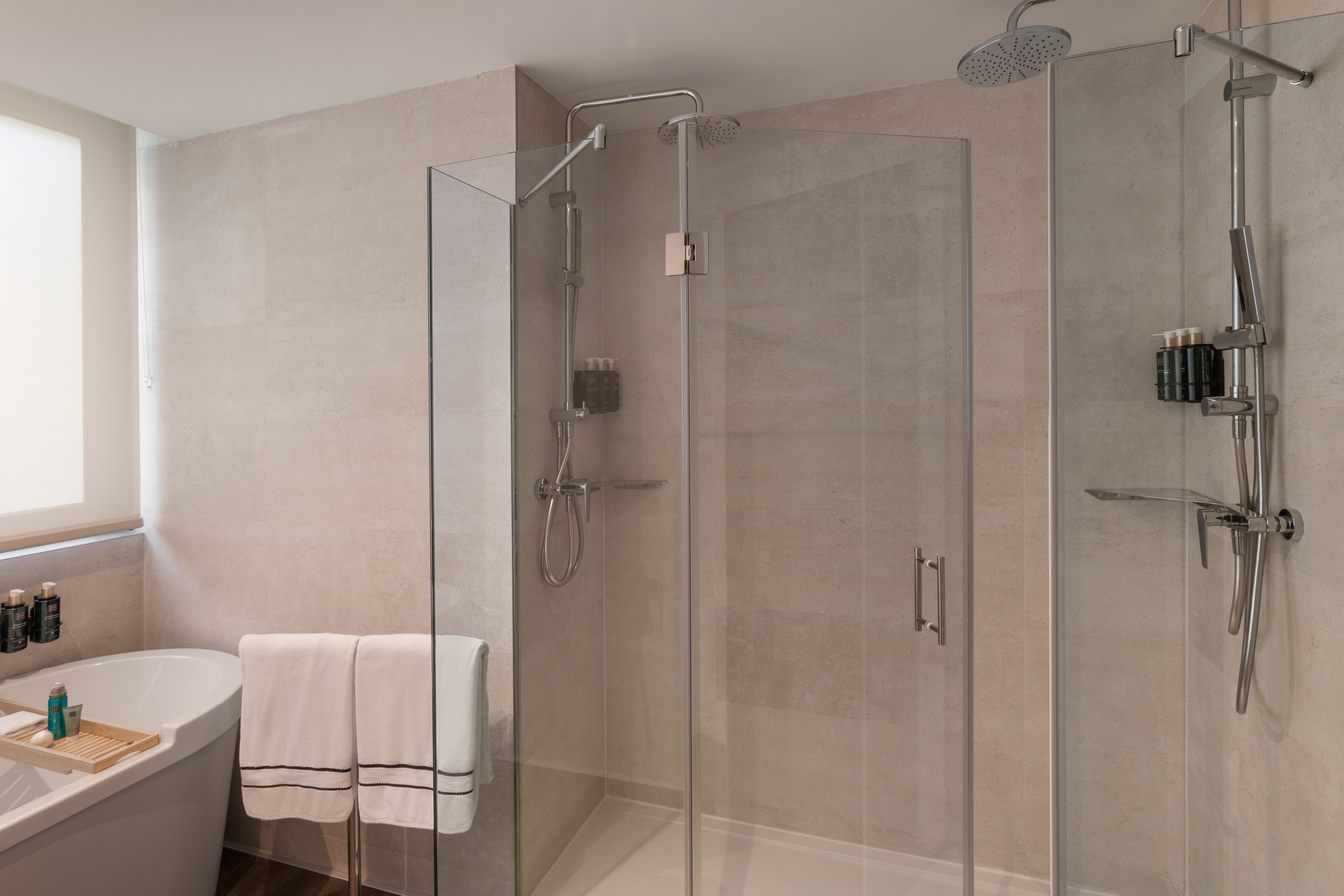Baño moderno con ducha de cristal, bañera, azulejos claros y toallas.