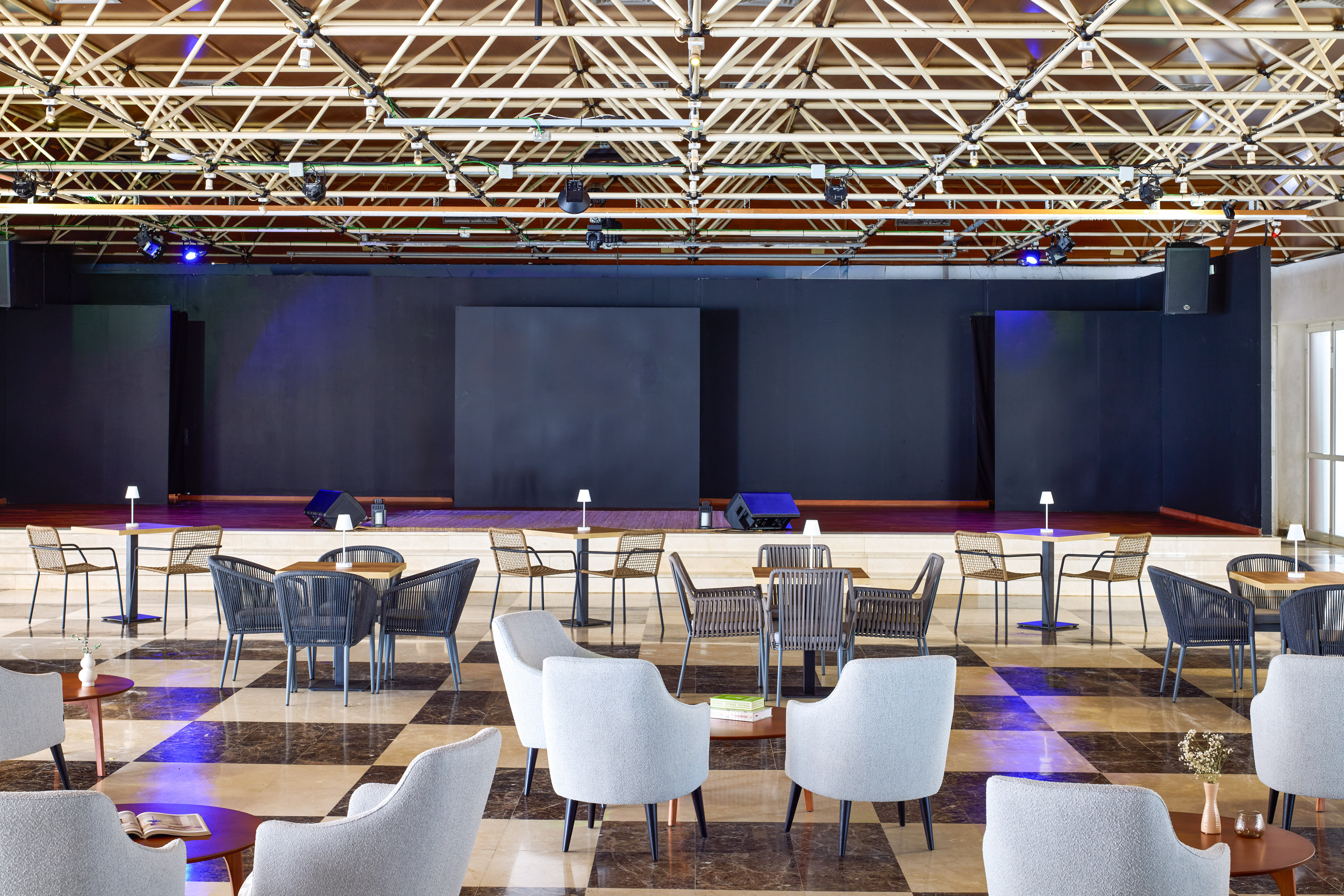 Modern event lounge with stage, mixed seating, and exposed truss ceiling.