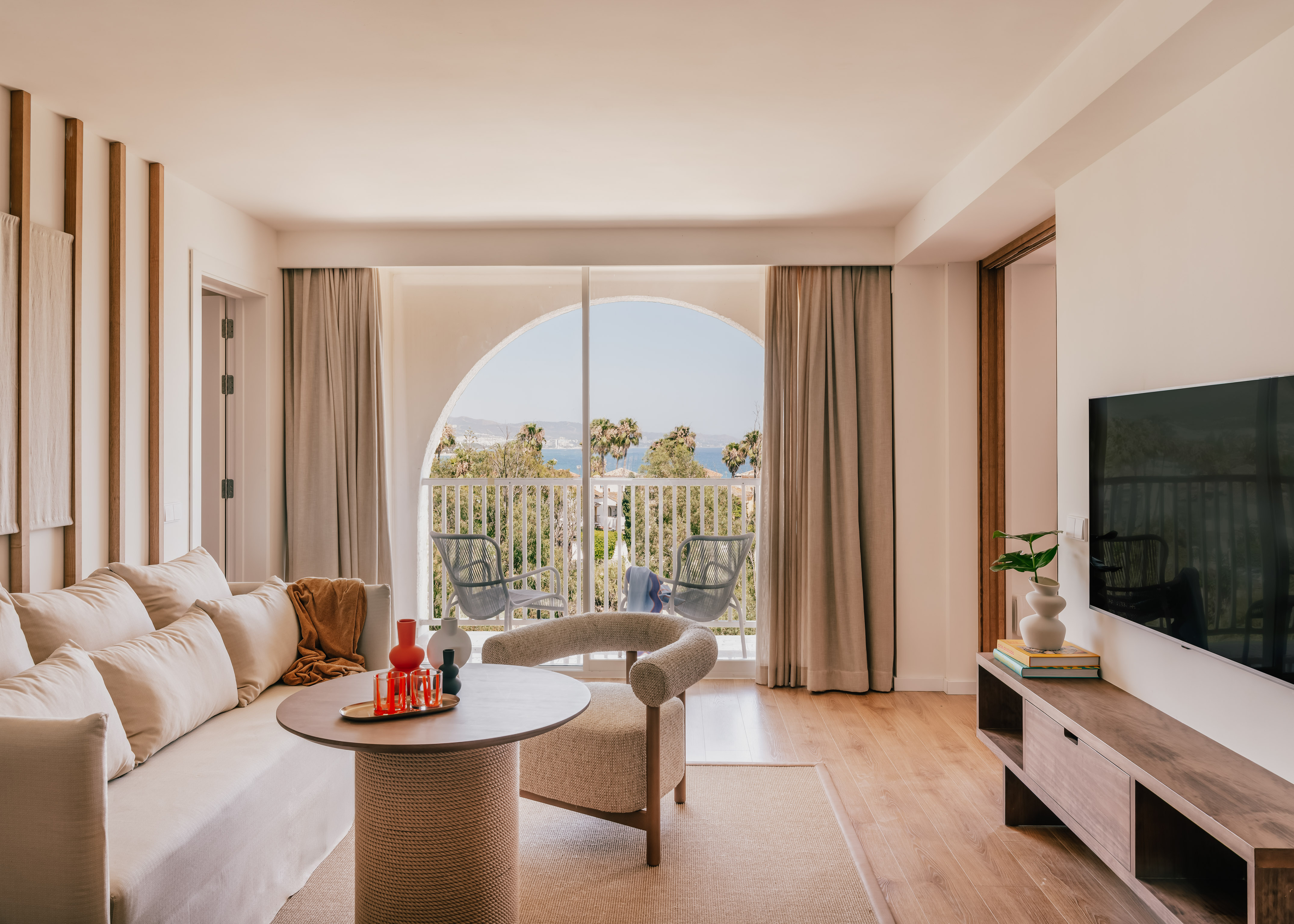 Modern living room with sea view balcony, sofa, and palm trees. Hotel suite.