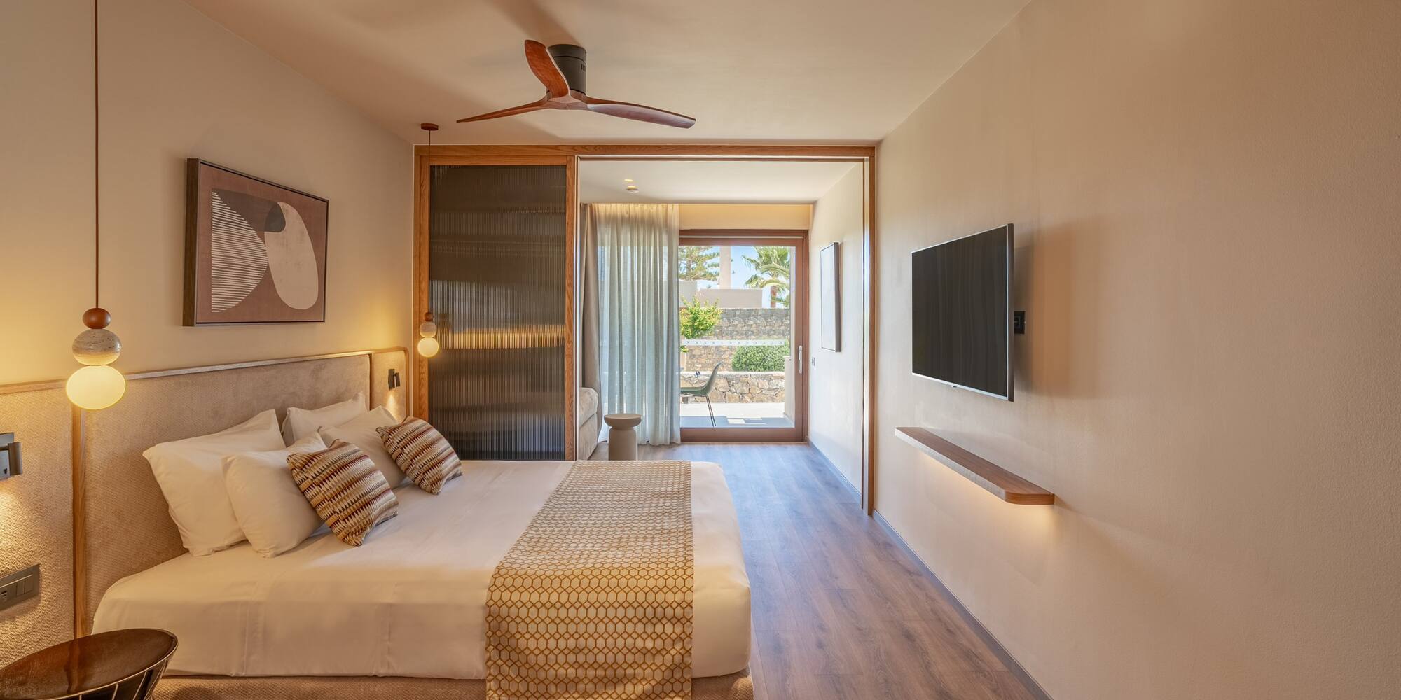 Modern hotel room with large bed, wood floor, ceiling fan, and patio view.