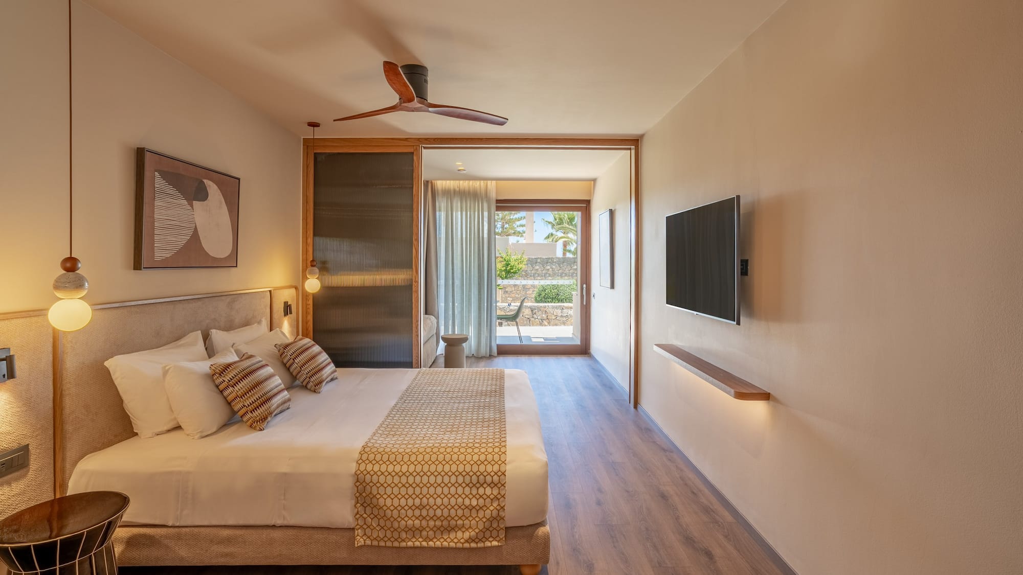 Modern hotel room with large bed, wood floor, ceiling fan, and patio view.
