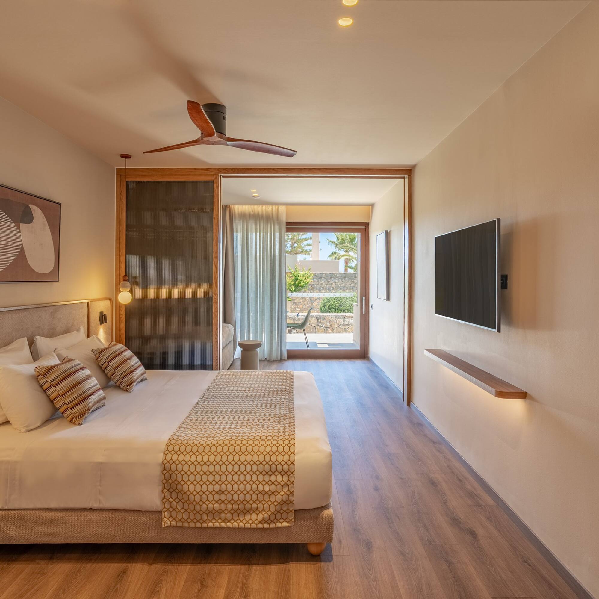 Modern hotel room with large bed, wood floor, ceiling fan, and patio view.