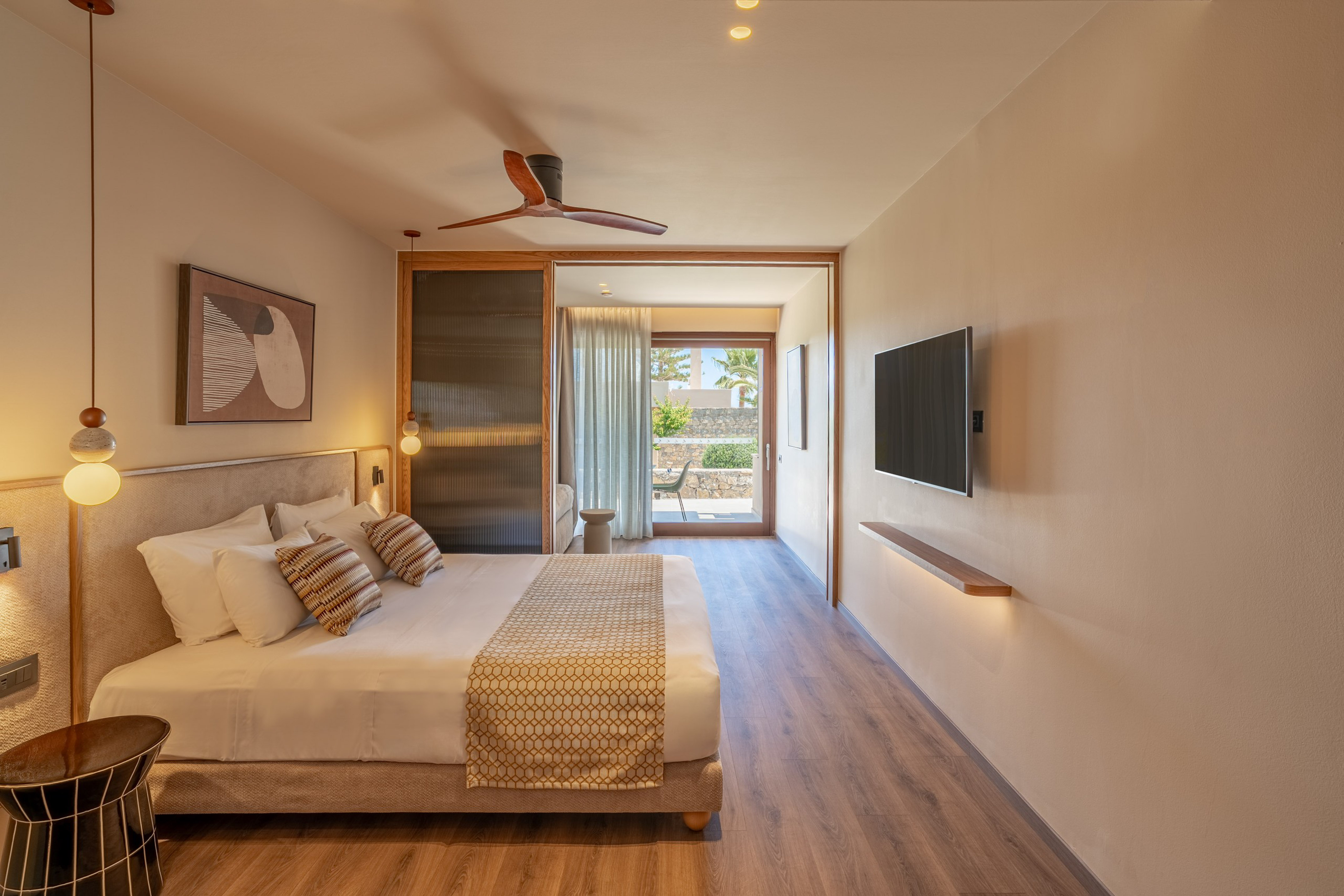 Modern hotel room with large bed, wood floor, ceiling fan, and patio view.