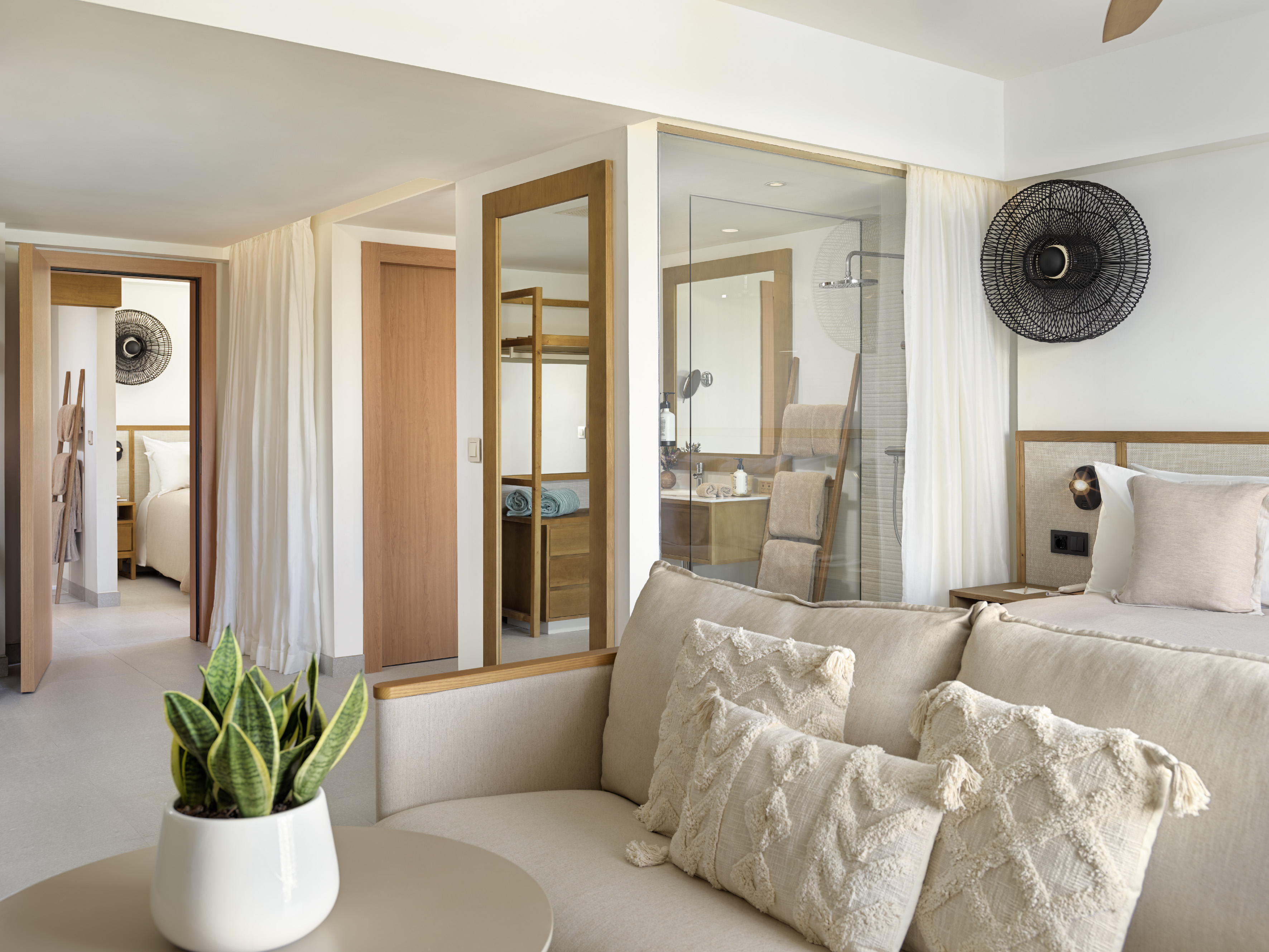 Neutral modern hotel suite with sofa, bed, and open concept bathroom.