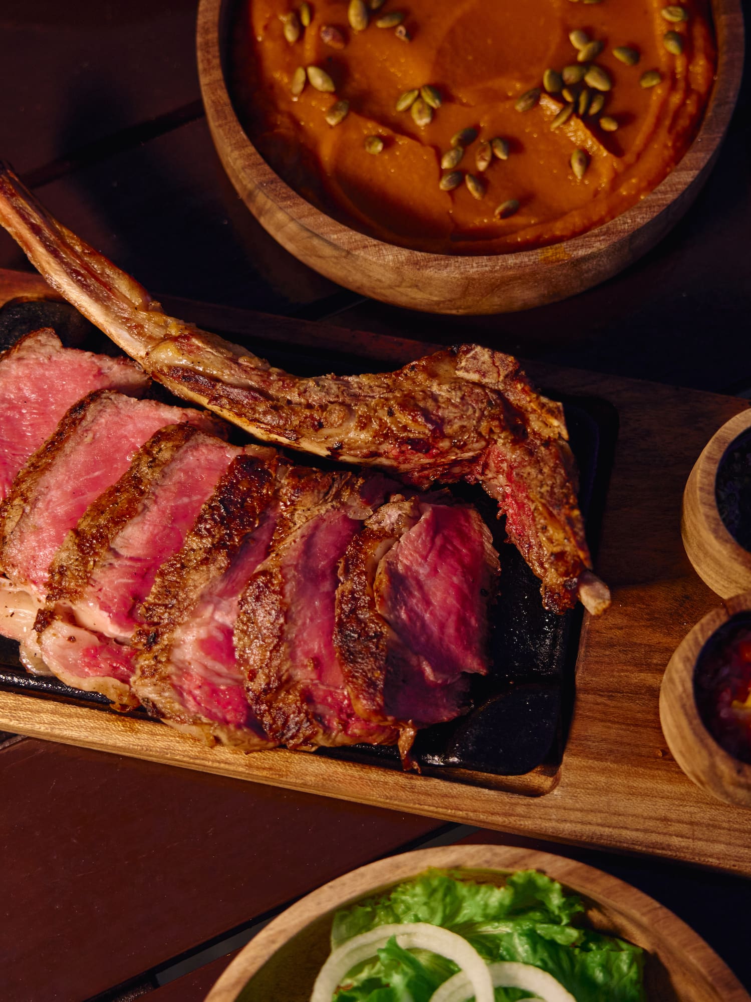 Tomahawk de res cortado con puré, ensalada y salsas en restaurante.