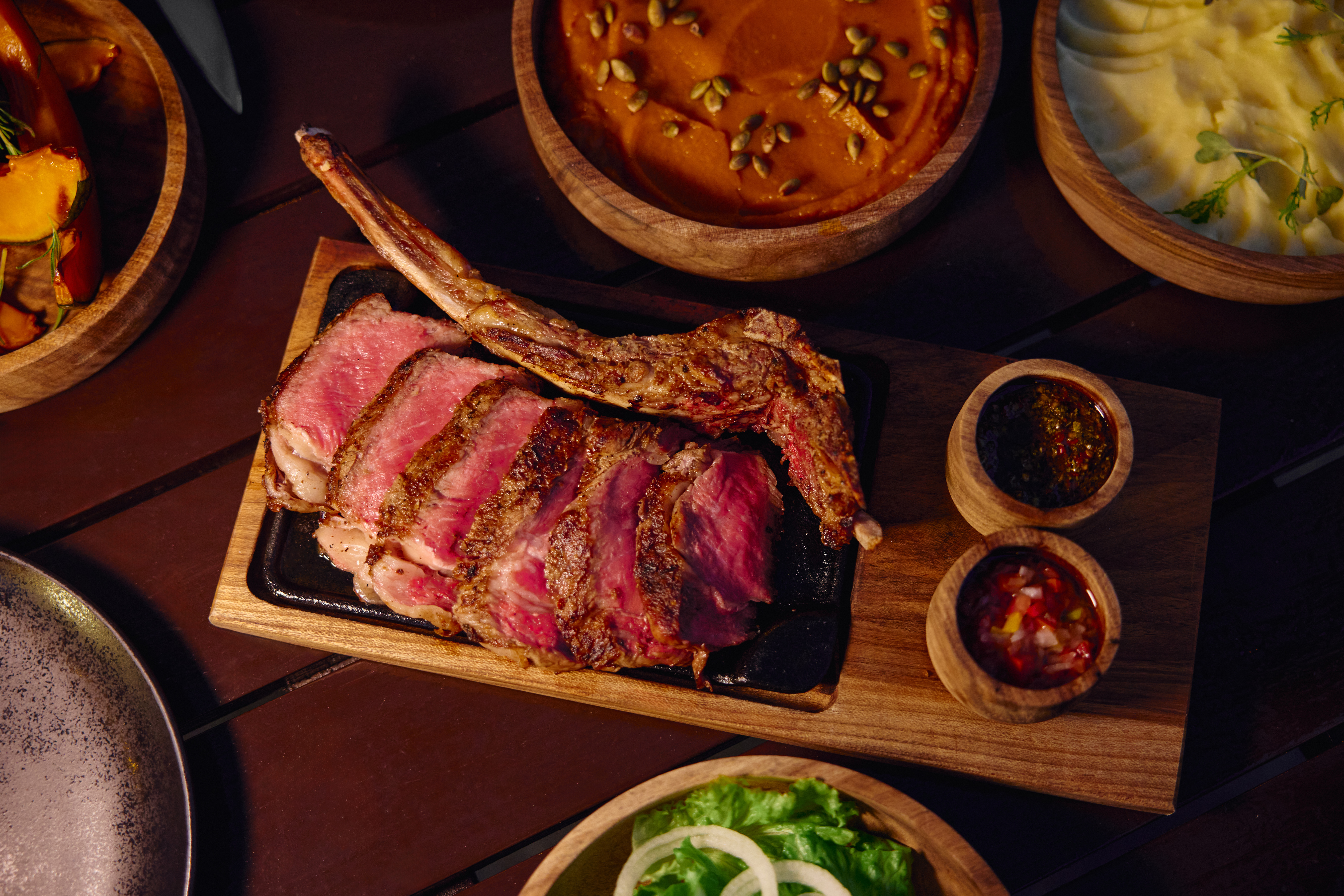Tomahawk de res cortado con puré, ensalada y salsas en restaurante.