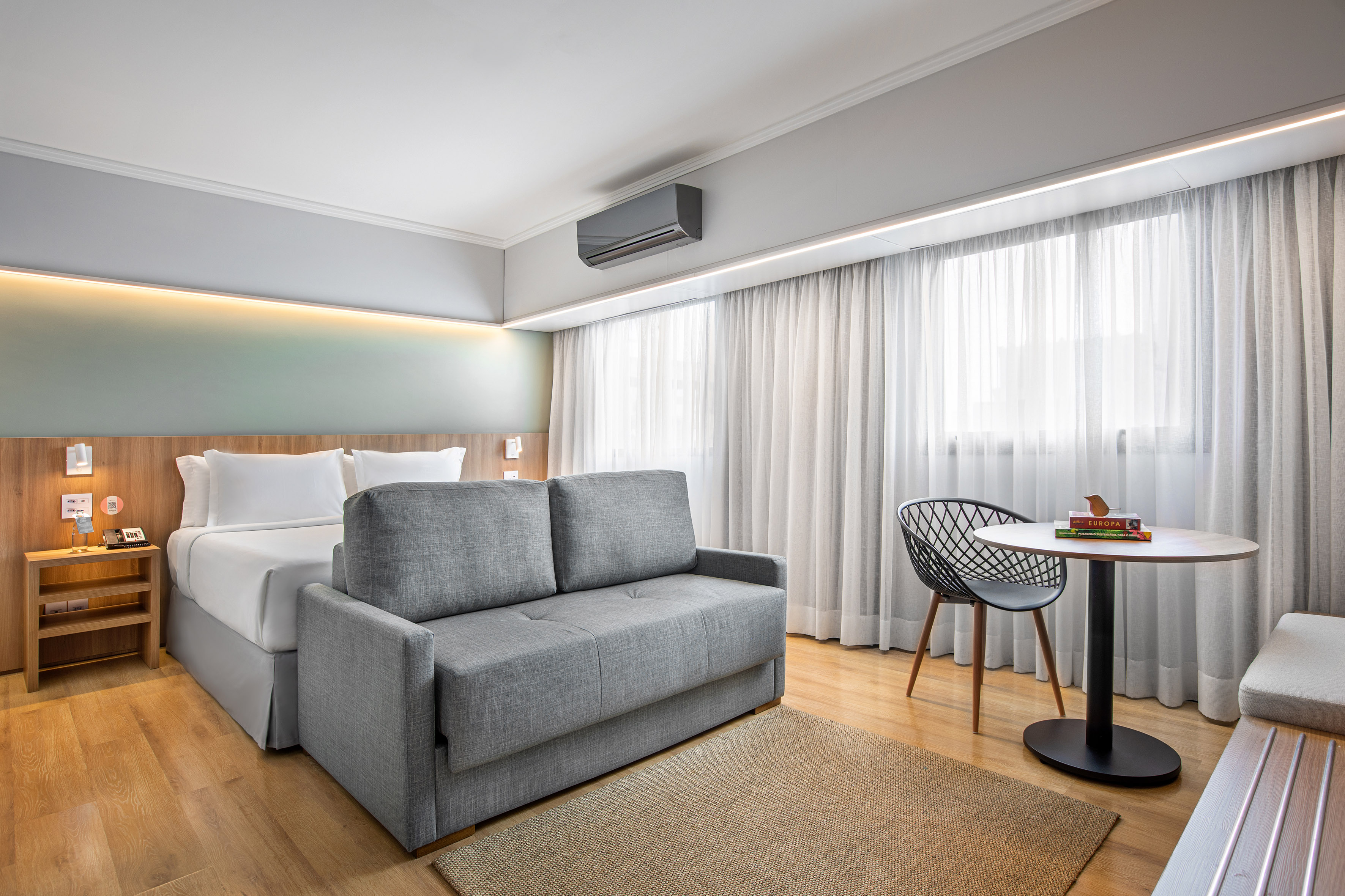 Modern hotel suite featuring a bed, gray sofa bed, and hardwood floor.