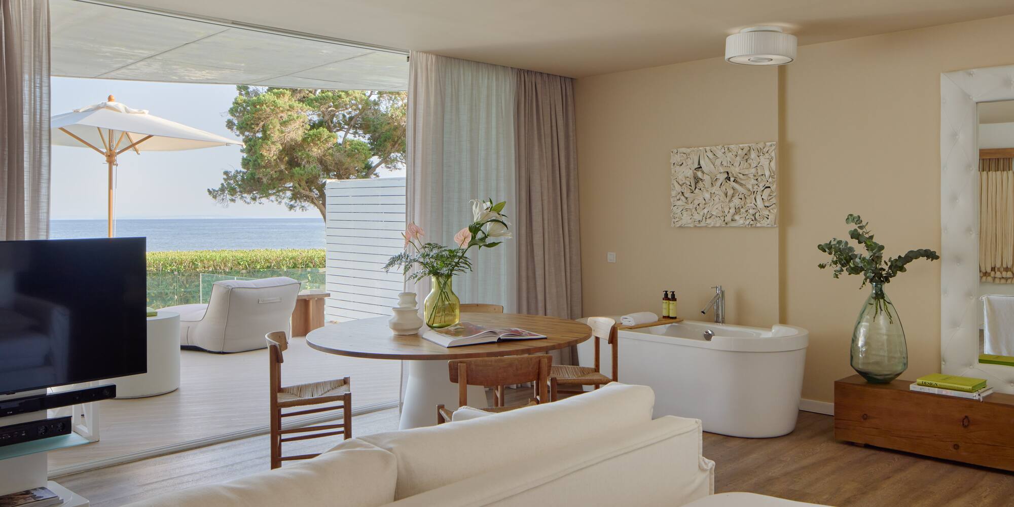 Oceanfront luxury suite with balcony, modern decor, and freestanding tub.