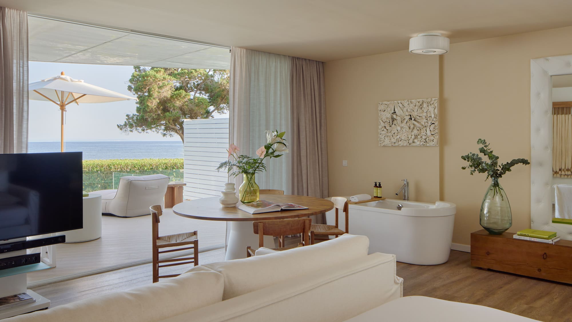 Oceanfront luxury suite with balcony, modern decor, and freestanding tub.