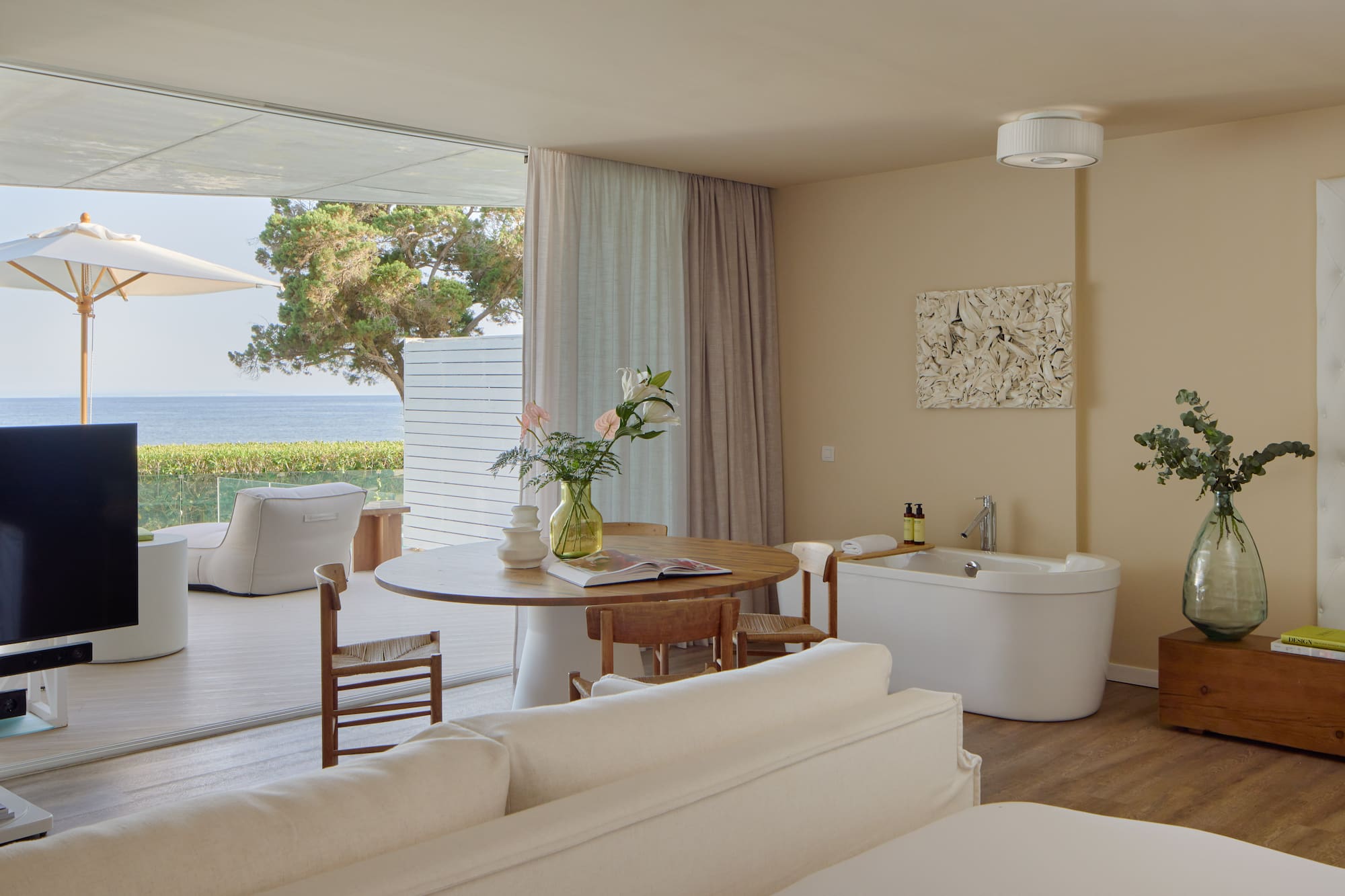 Oceanfront luxury suite with balcony, modern decor, and freestanding tub.