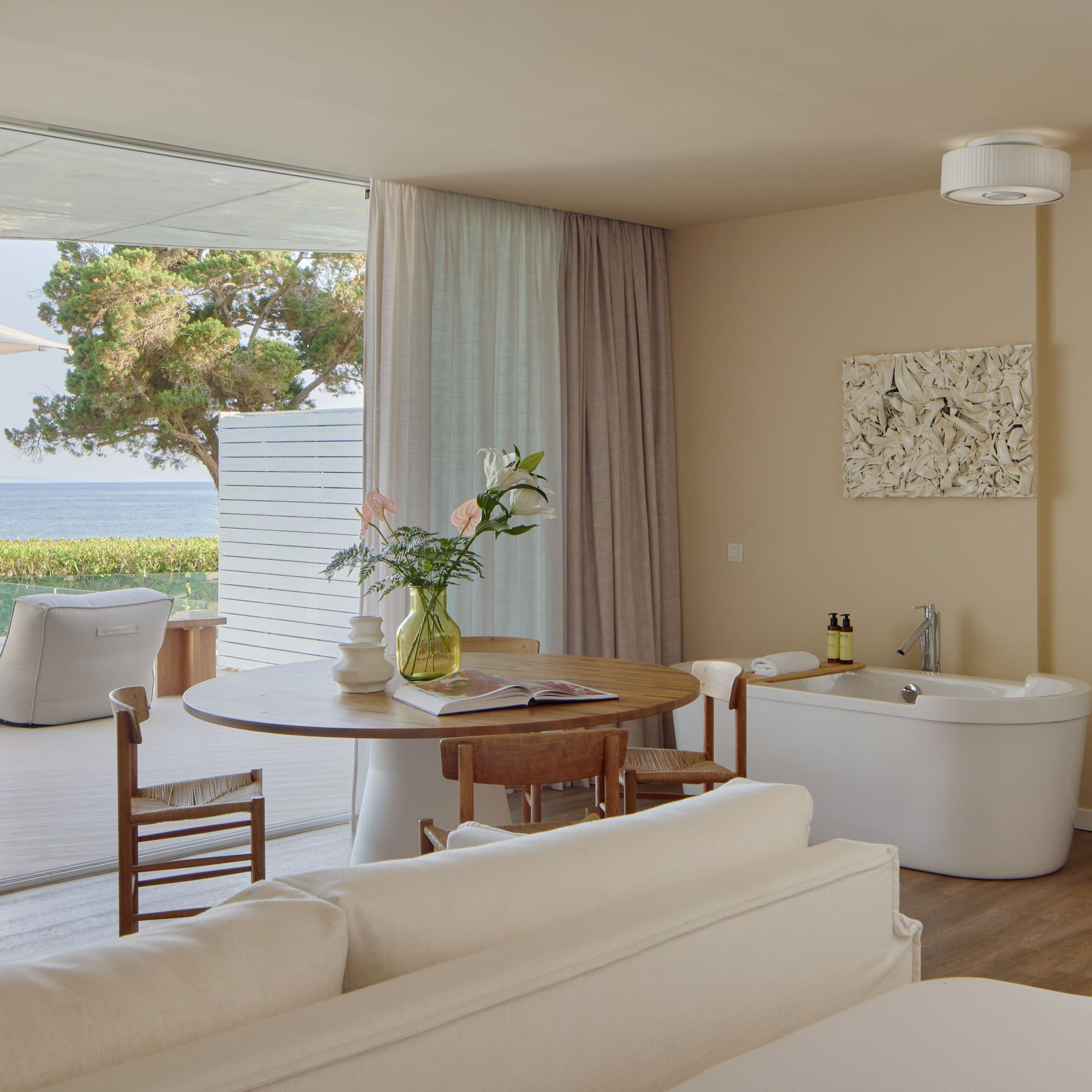 Oceanfront luxury suite with balcony, modern decor, and freestanding tub.