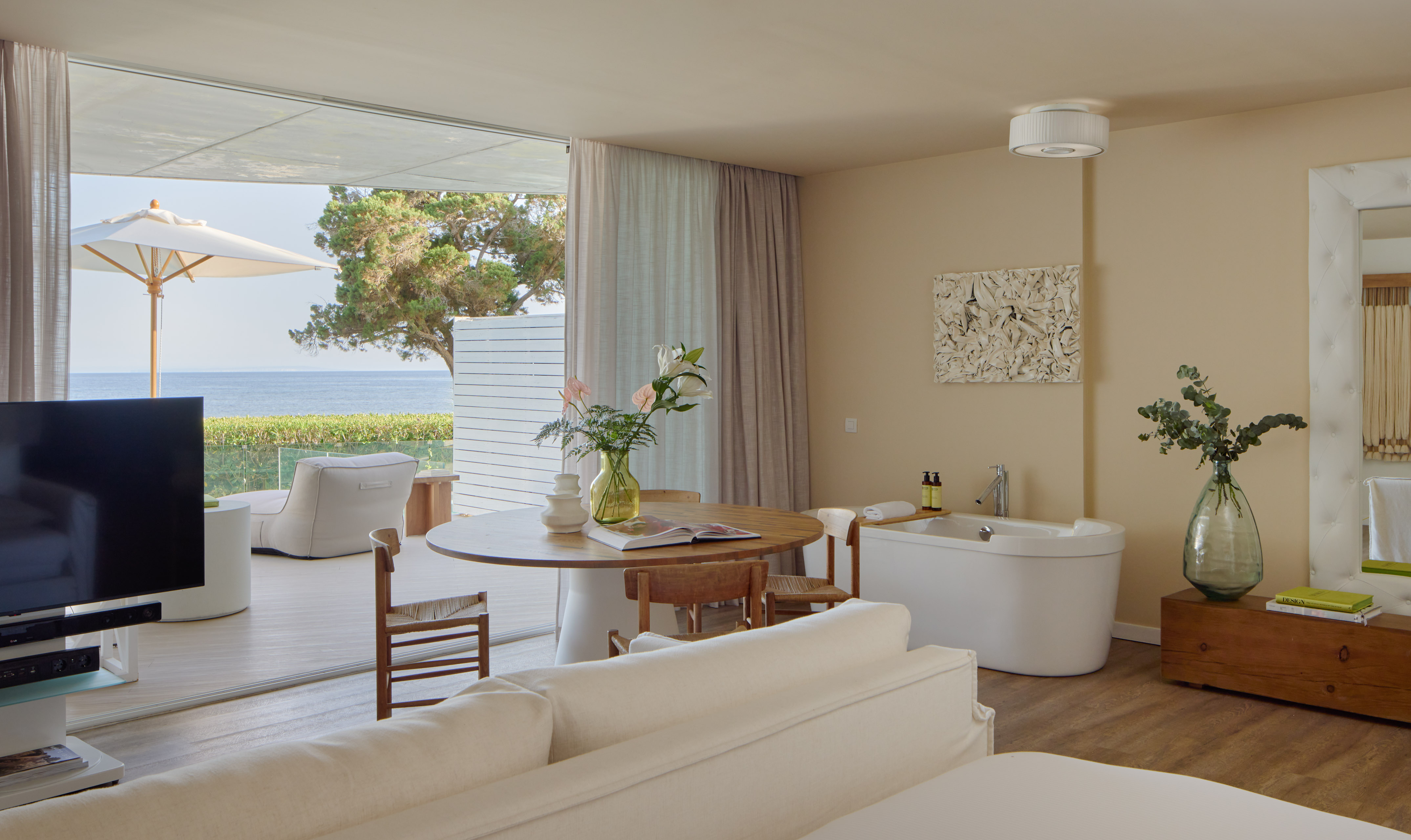 Oceanfront luxury suite with balcony, modern decor, and freestanding tub.