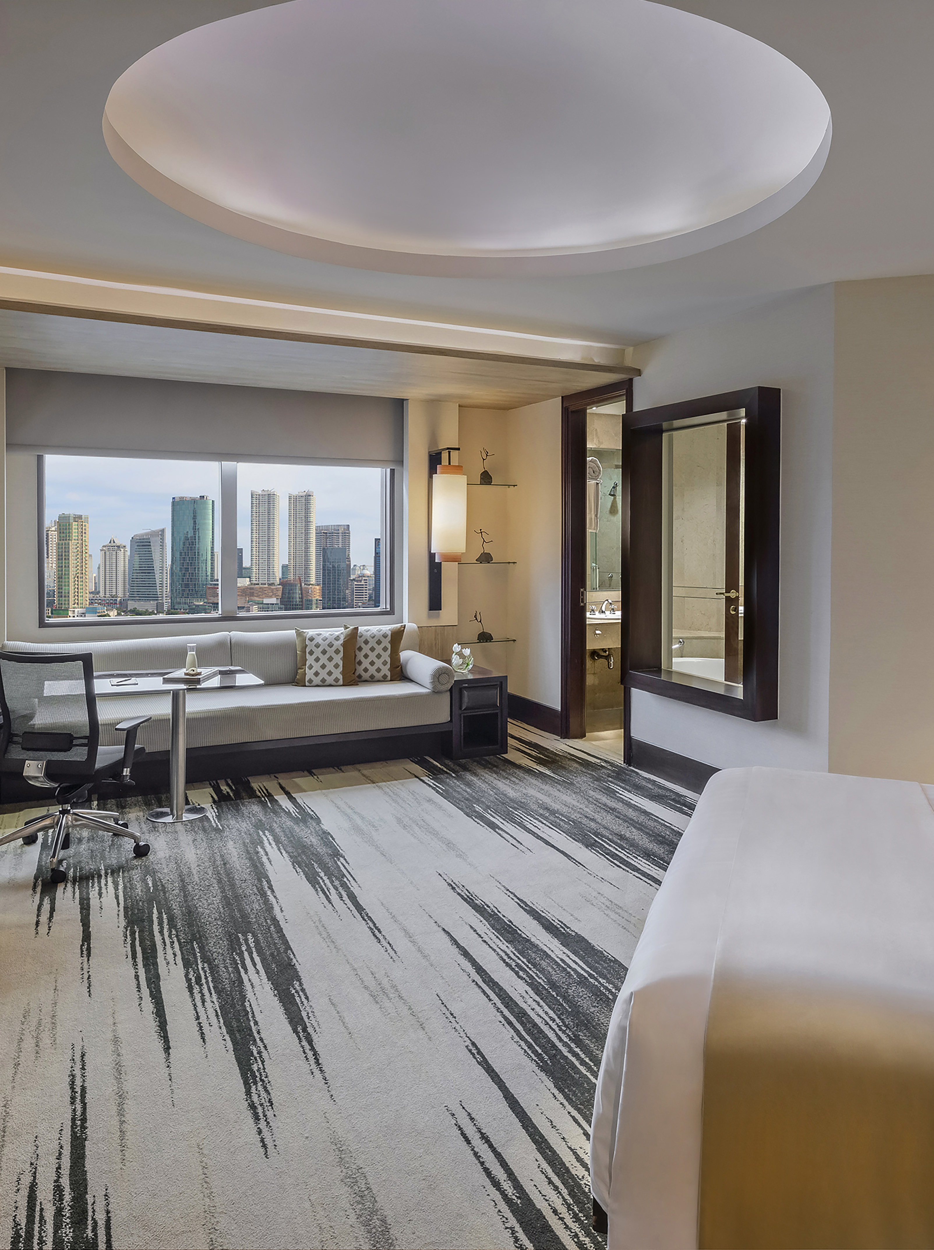 Luxury hotel suite with city skyline view, desk, lounge, and abstract rug.