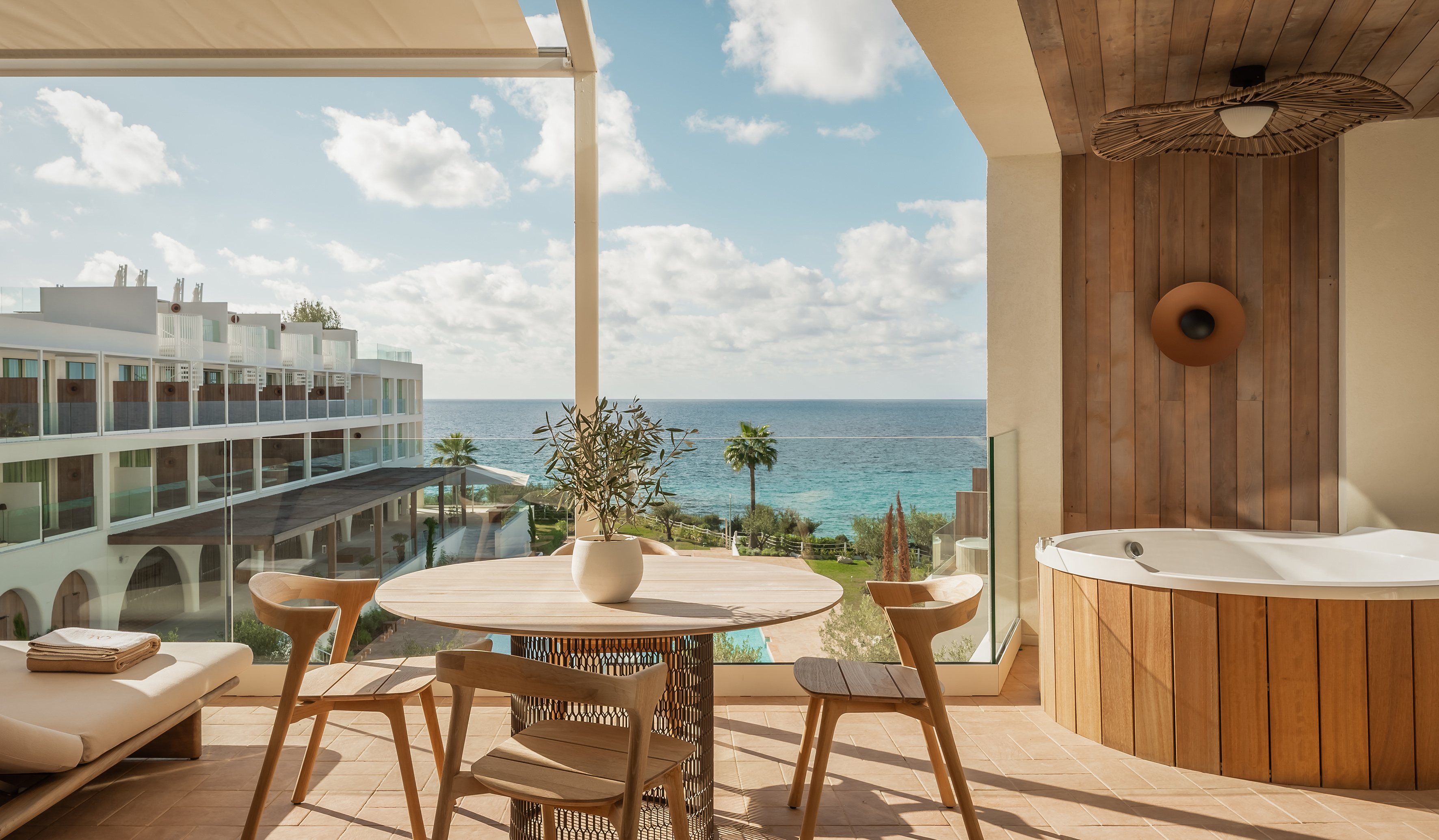 Modern hotel balcony with sea view, private hot tub, and dining table.