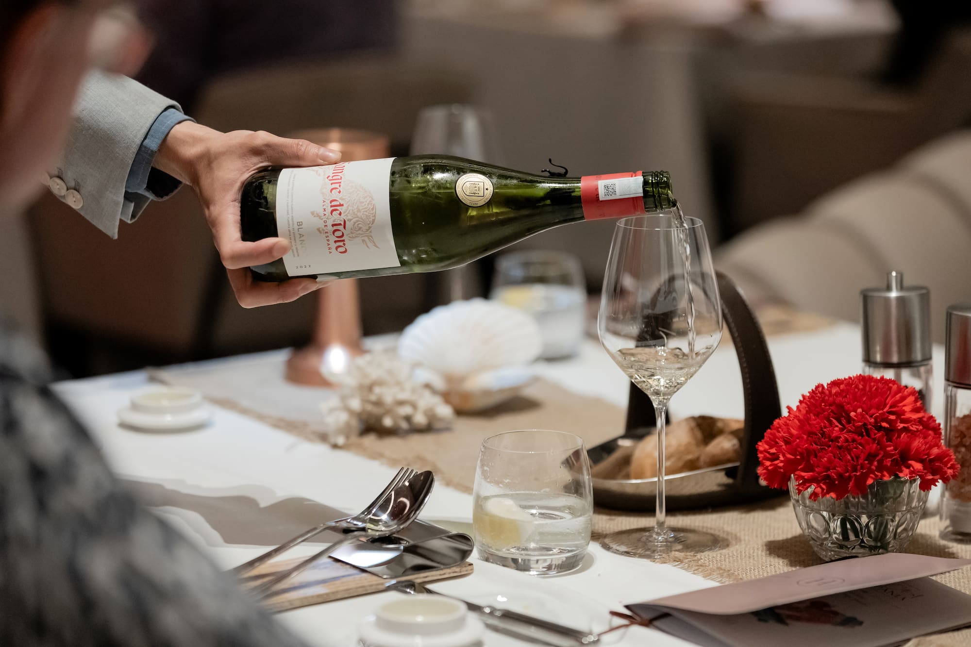 White wine from a Sangre de Toro bottle poured into a glass at a dinner table.