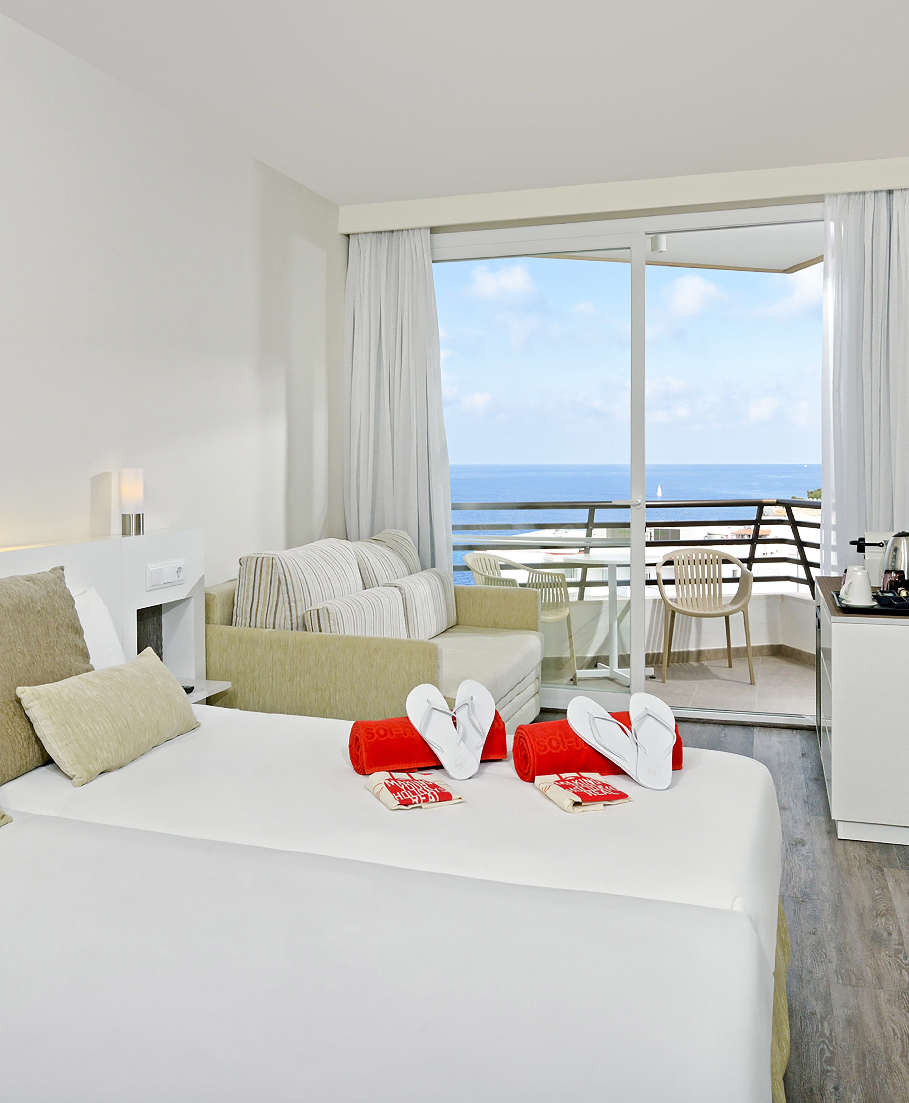 Bright hotel room with ocean view balcony, bed, sofa, and beach amenities.