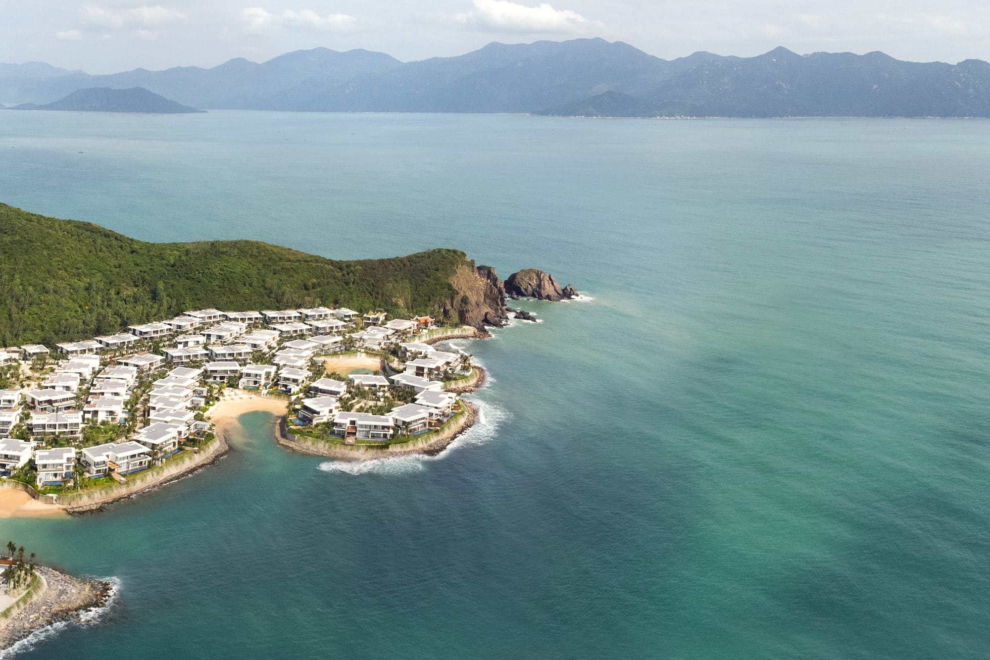 Modern coastal resort and villas on green hills by turquoise ocean.