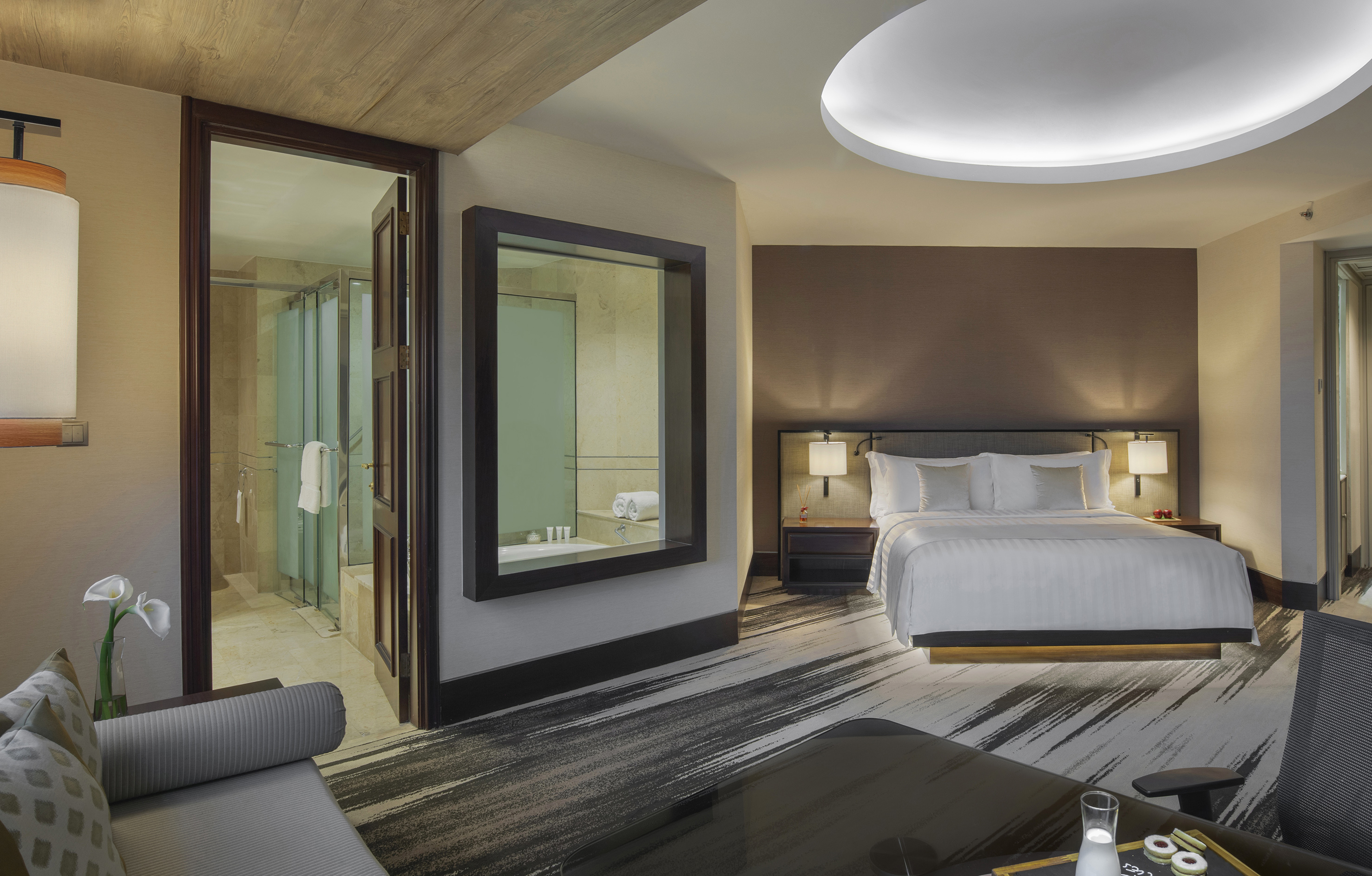 Luxury hotel suite with king bed, modern design, and visible bathroom.