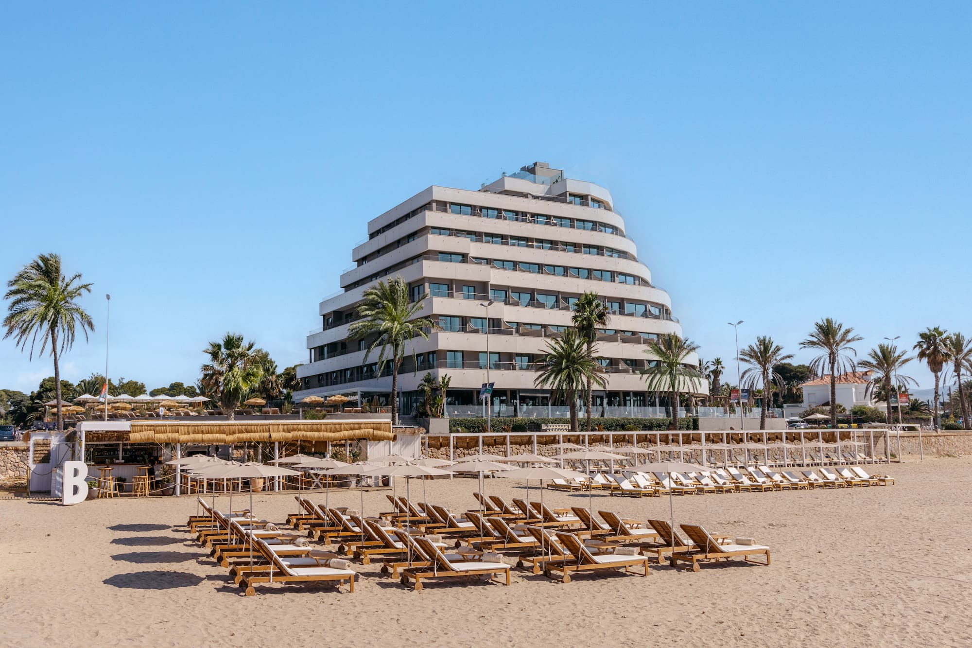 Modern tiered beachfront hotel with lounge chairs and palm trees.