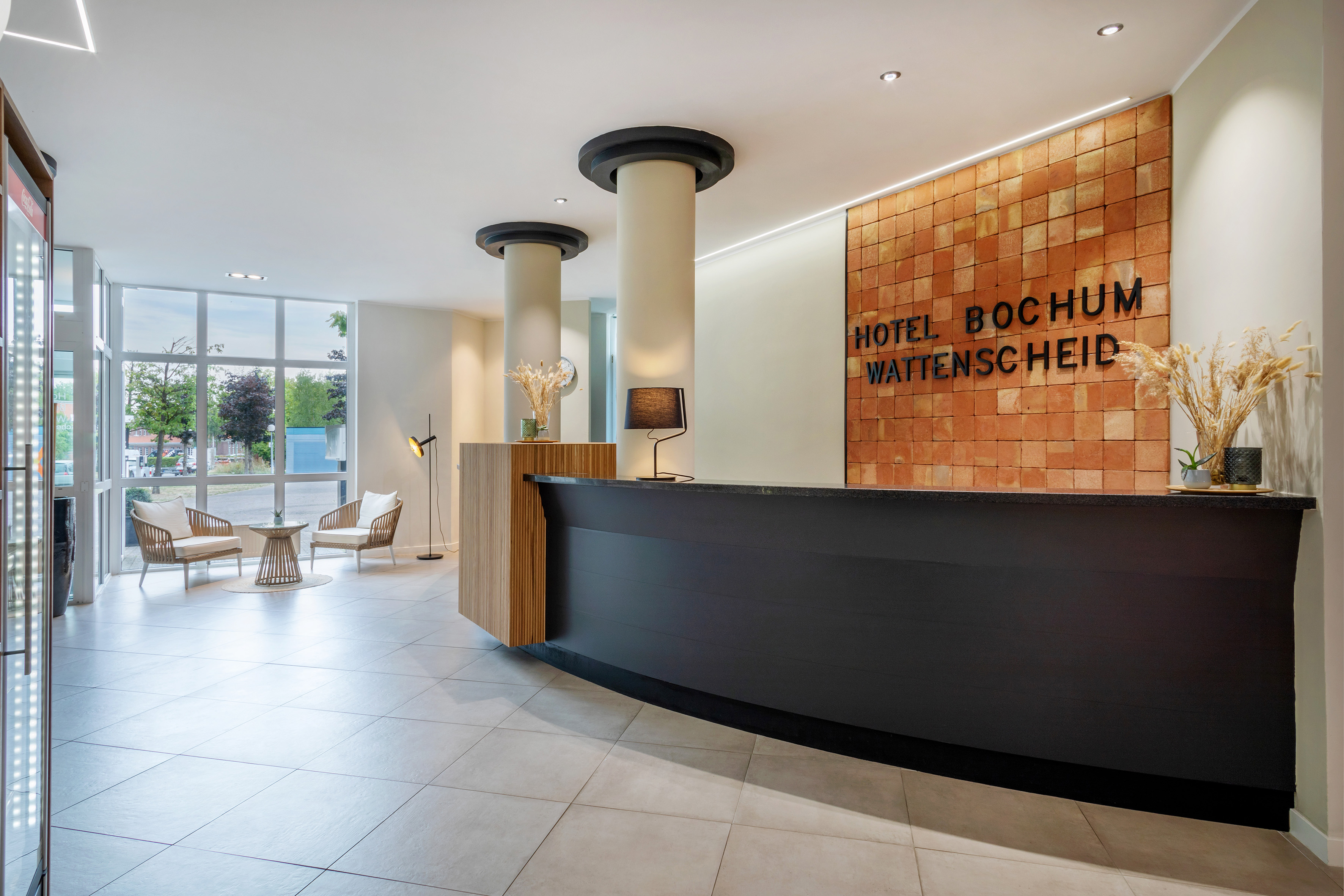 Modern hotel lobby with black reception desk and "Hotel Bochum Wattenscheid" sign.