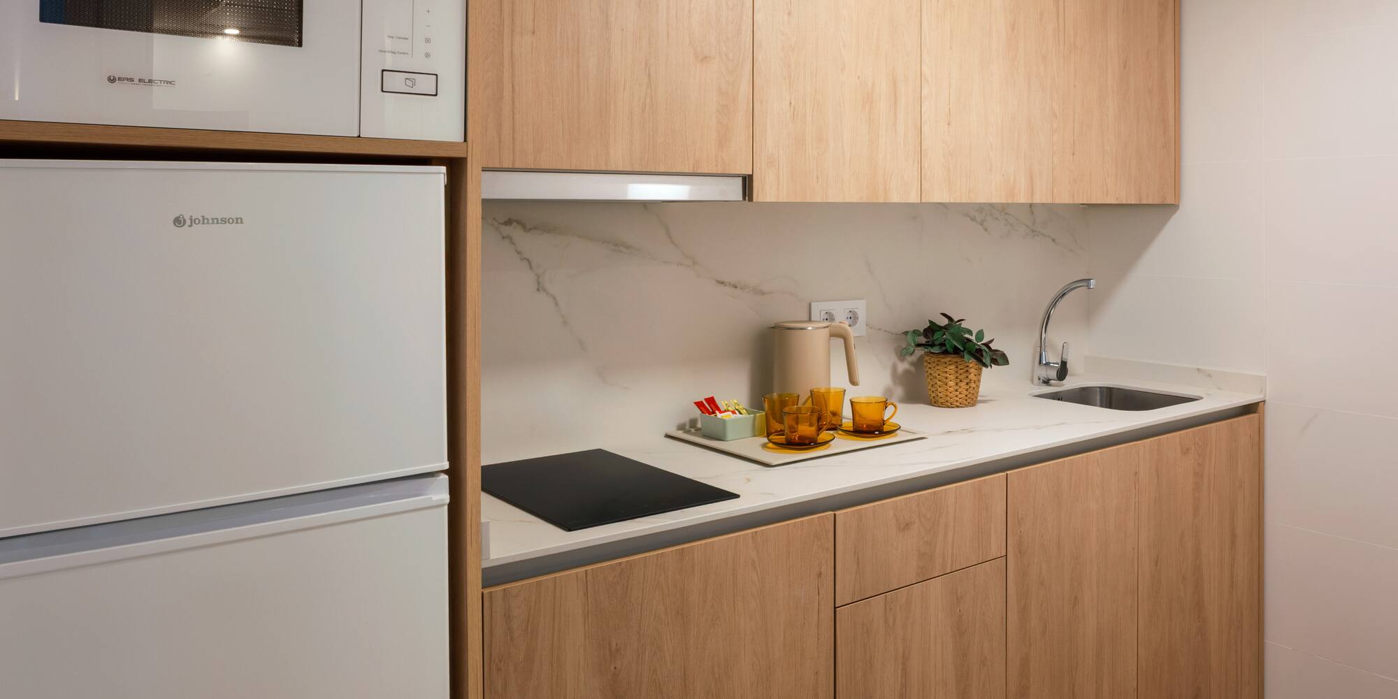 Modern compact kitchen with light wood cabinets, white appliances, marble counter.