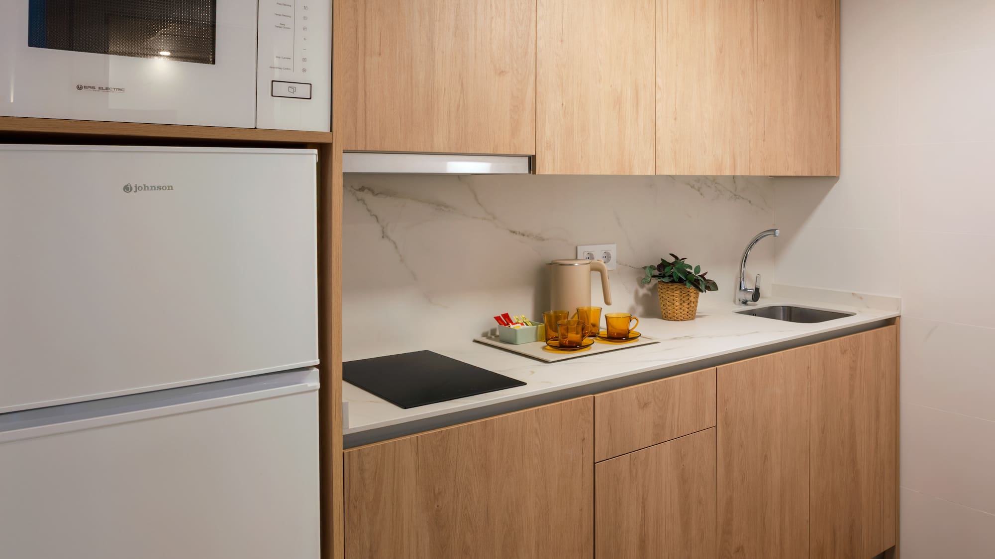 Modern compact kitchen with light wood cabinets, white appliances, marble counter.