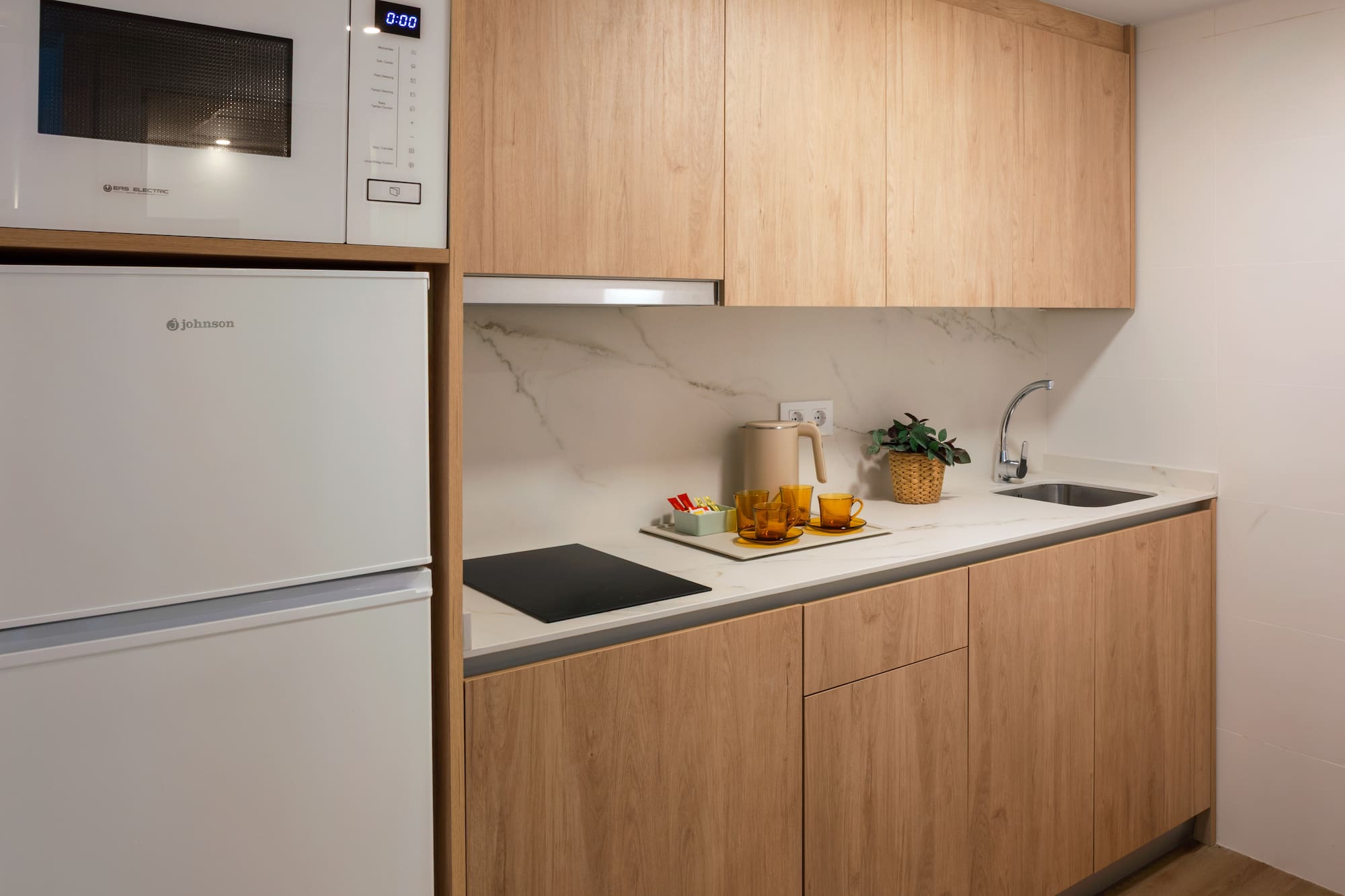 Modern kitchenette with wood cabinets, white appliances, and marble counter.