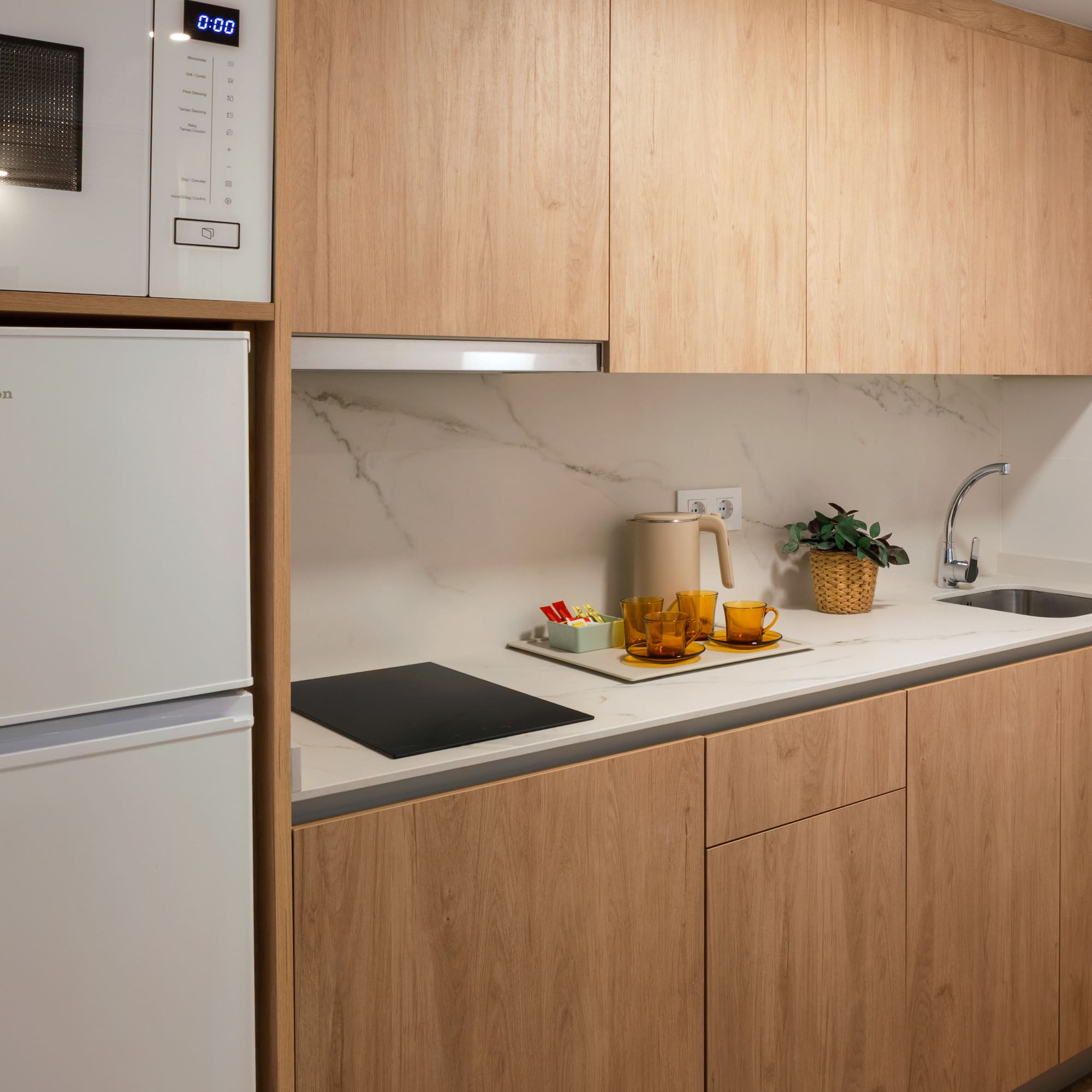 Modern compact kitchen with light wood cabinets, white appliances, marble counter.