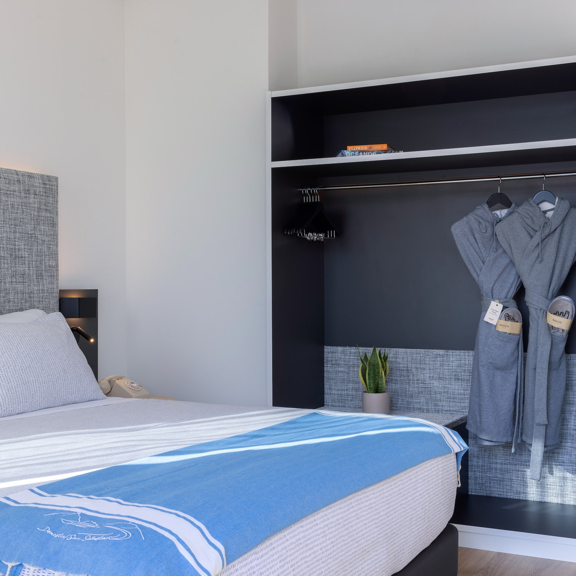 Dormitorio hotel moderno: cama, manta azul y armario con batas.