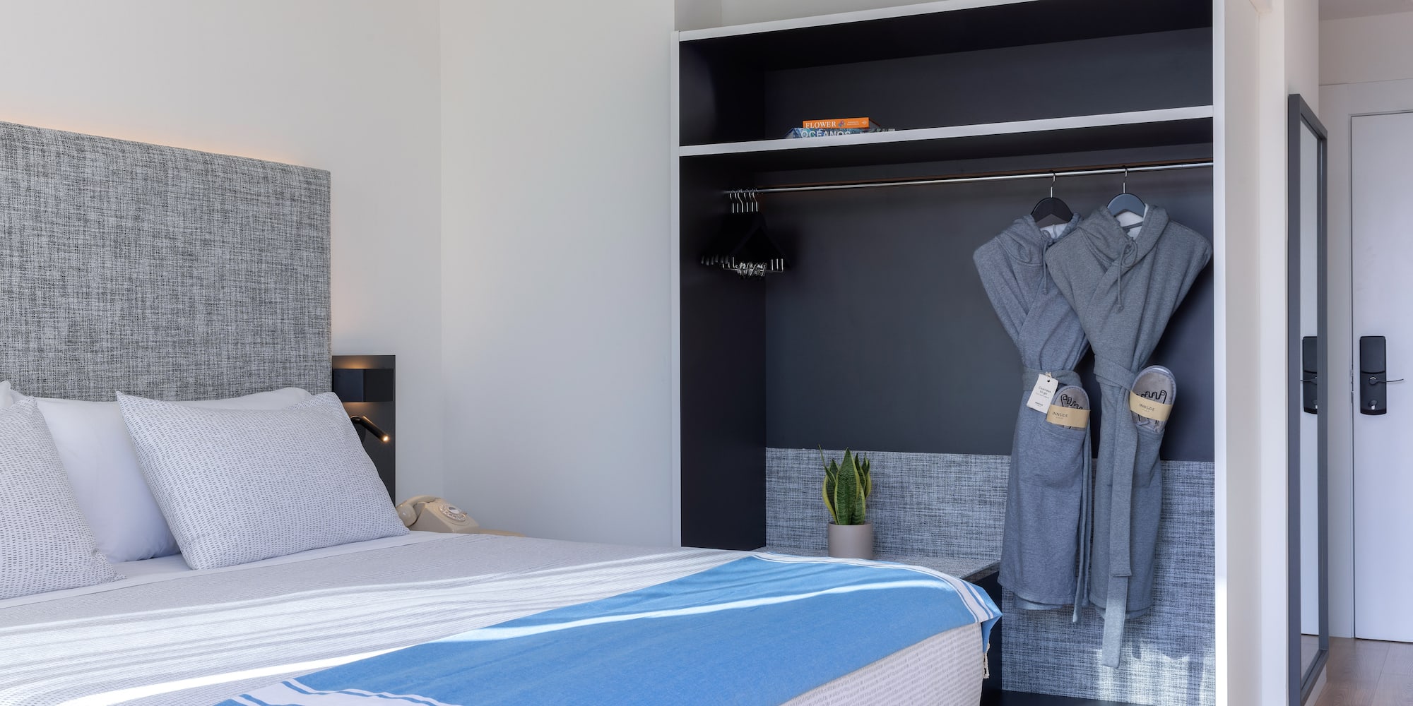 Dormitorio hotel moderno: cama, manta azul y armario con batas.