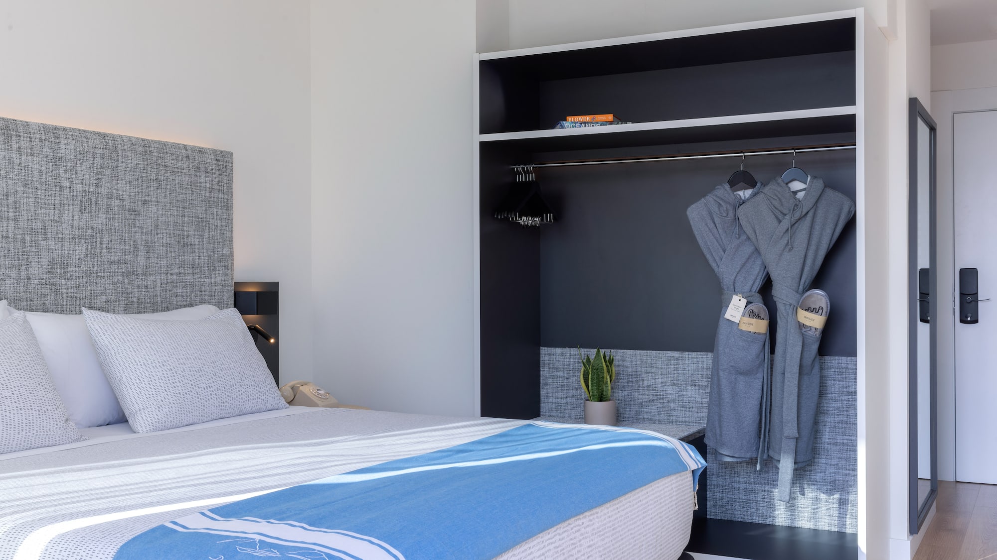 Dormitorio hotel moderno: cama, manta azul y armario con batas.